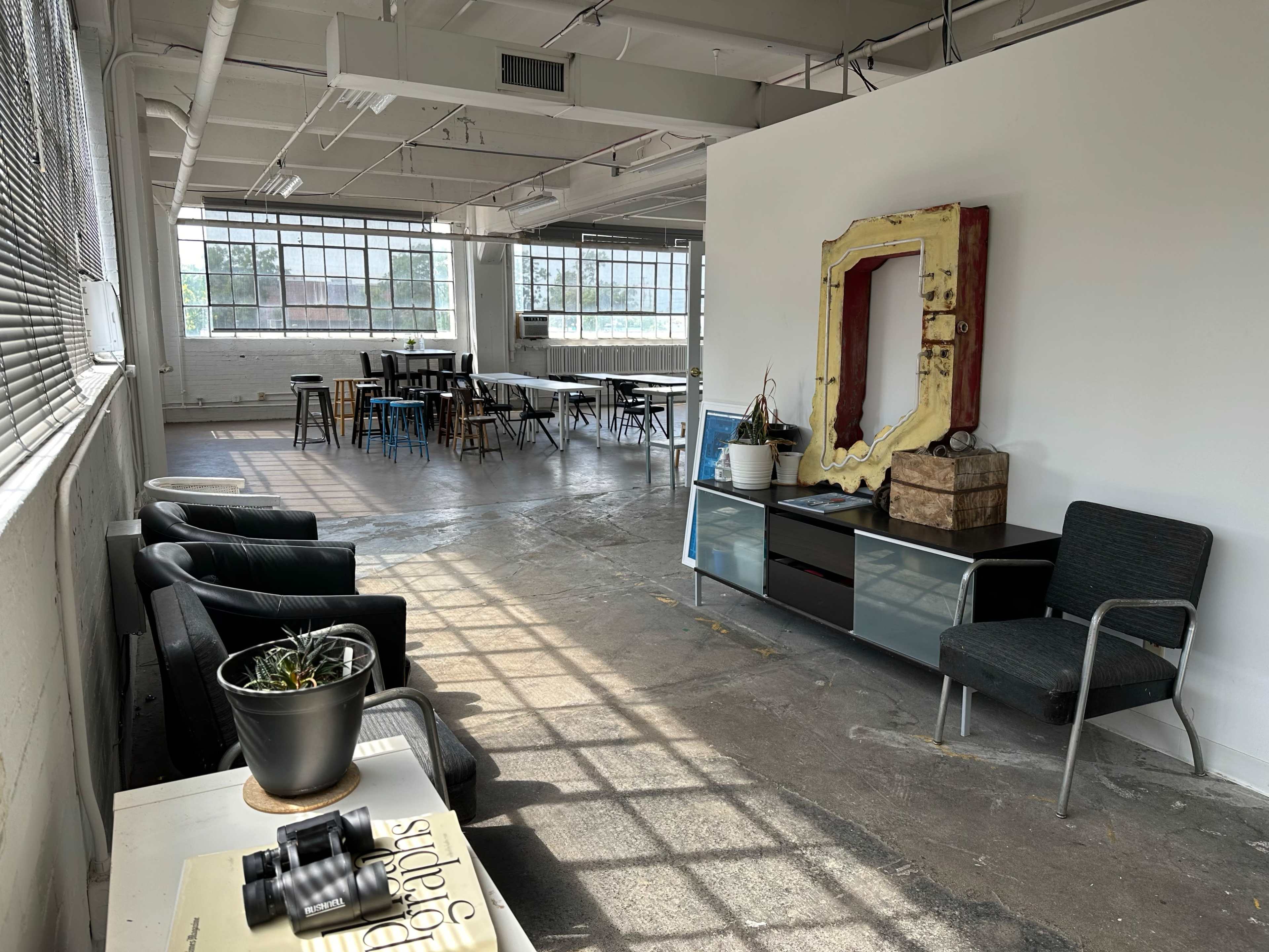 The image shows a spacious, well-lit industrial room with a seating area, a large table setup, and decorative elements along the walls.