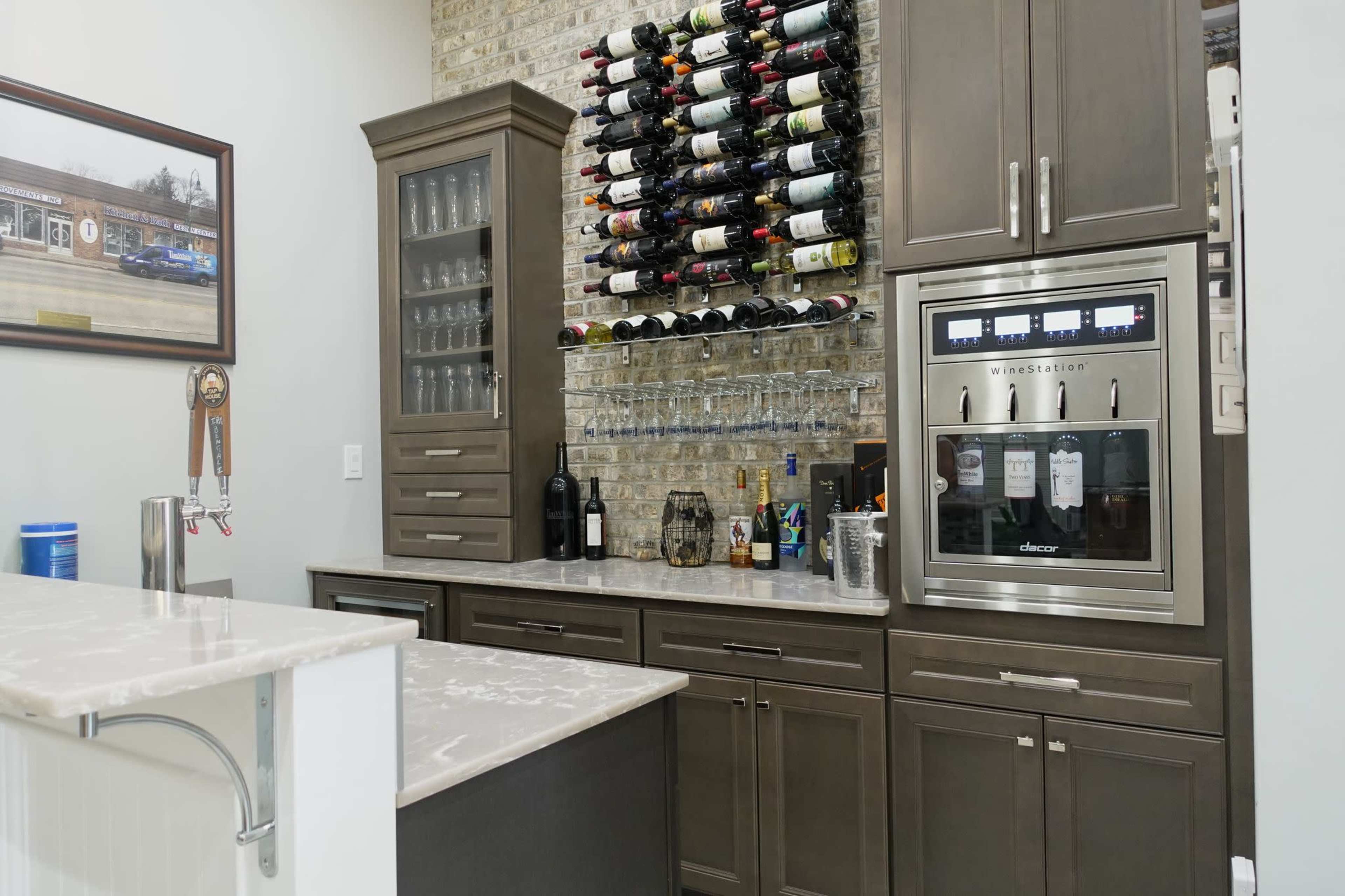 A modern home bar with a wine rack, glassware, and an appliance for beverage chilling, all set against a brick wall.
