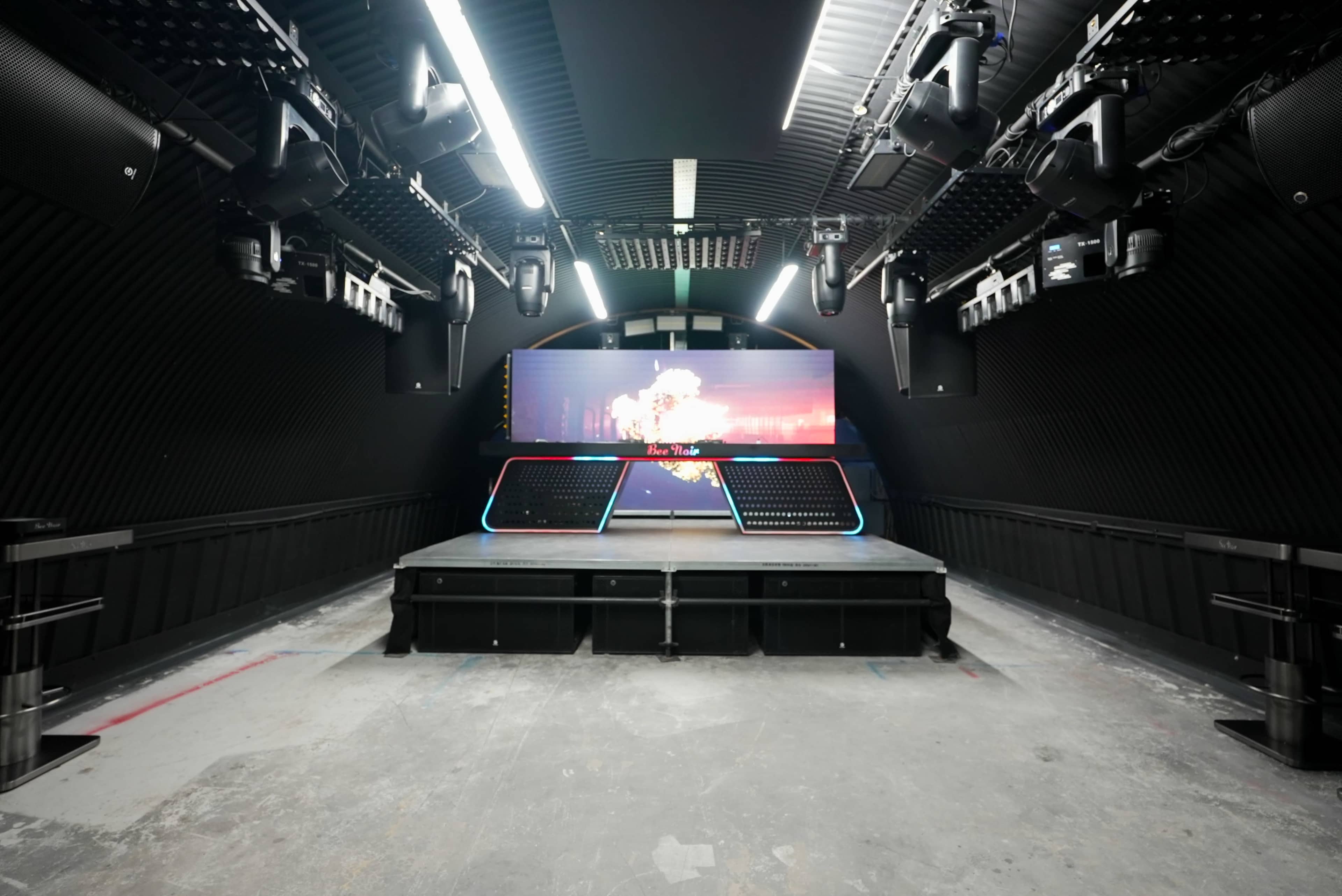 The image shows an empty performance stage with a large digital screen and audio equipment installed on the walls and ceiling.