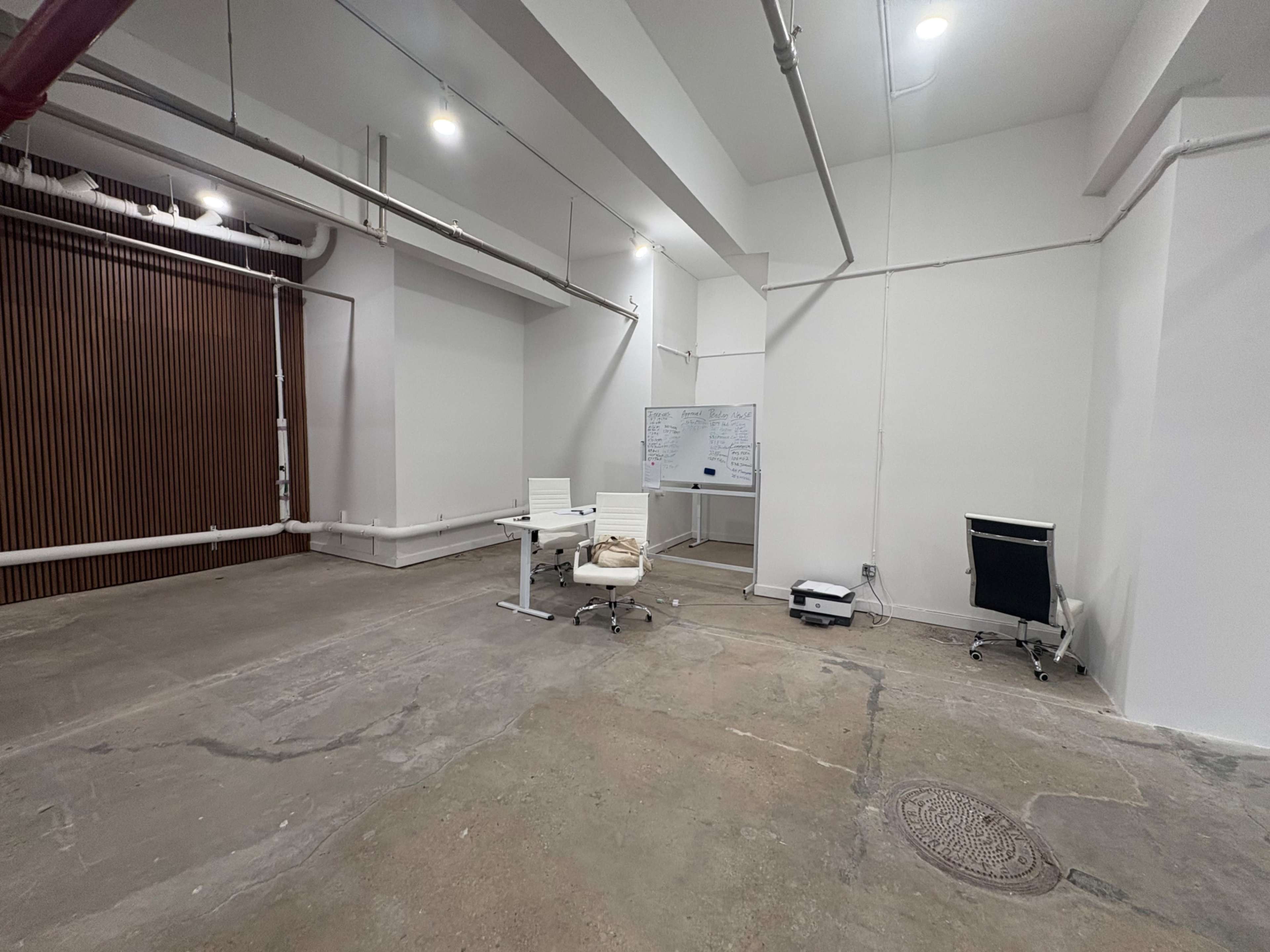 The image shows a spacious, minimally furnished office area with a desk, chair, whiteboard, and empty space.