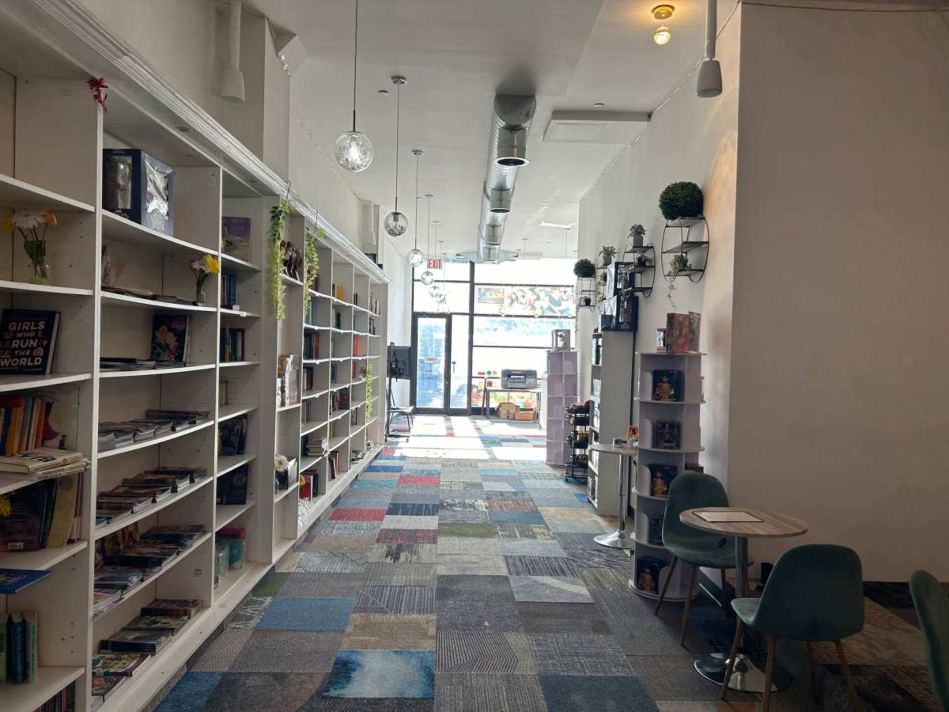 A hallway lined with bookshelves on each side, leading to a brightly lit entrance with a display screen visible at the end.