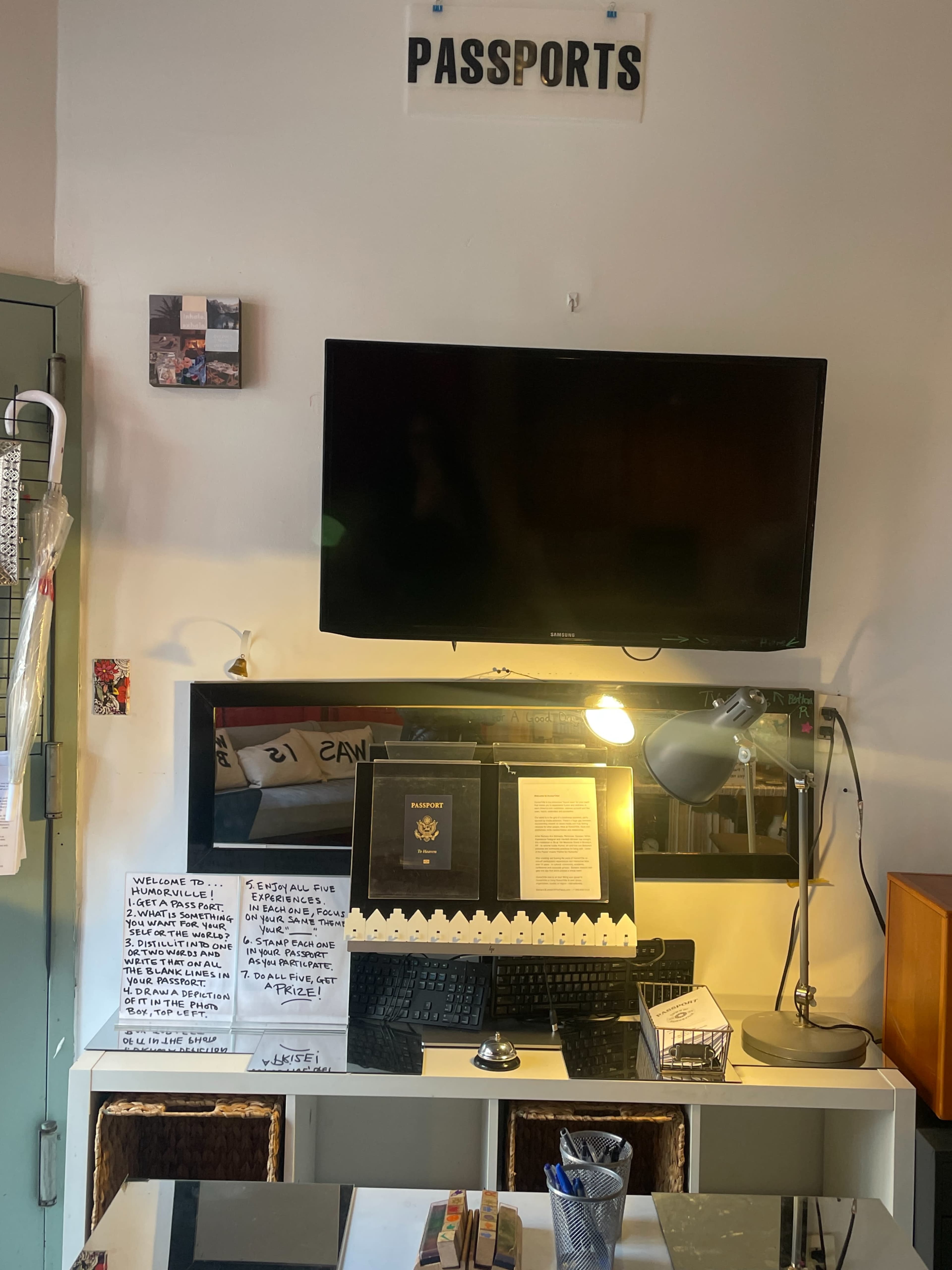 The image shows a desk with a television mounted above it, cluttered with documents, a keyboard, a lamp, and a storage basket.
