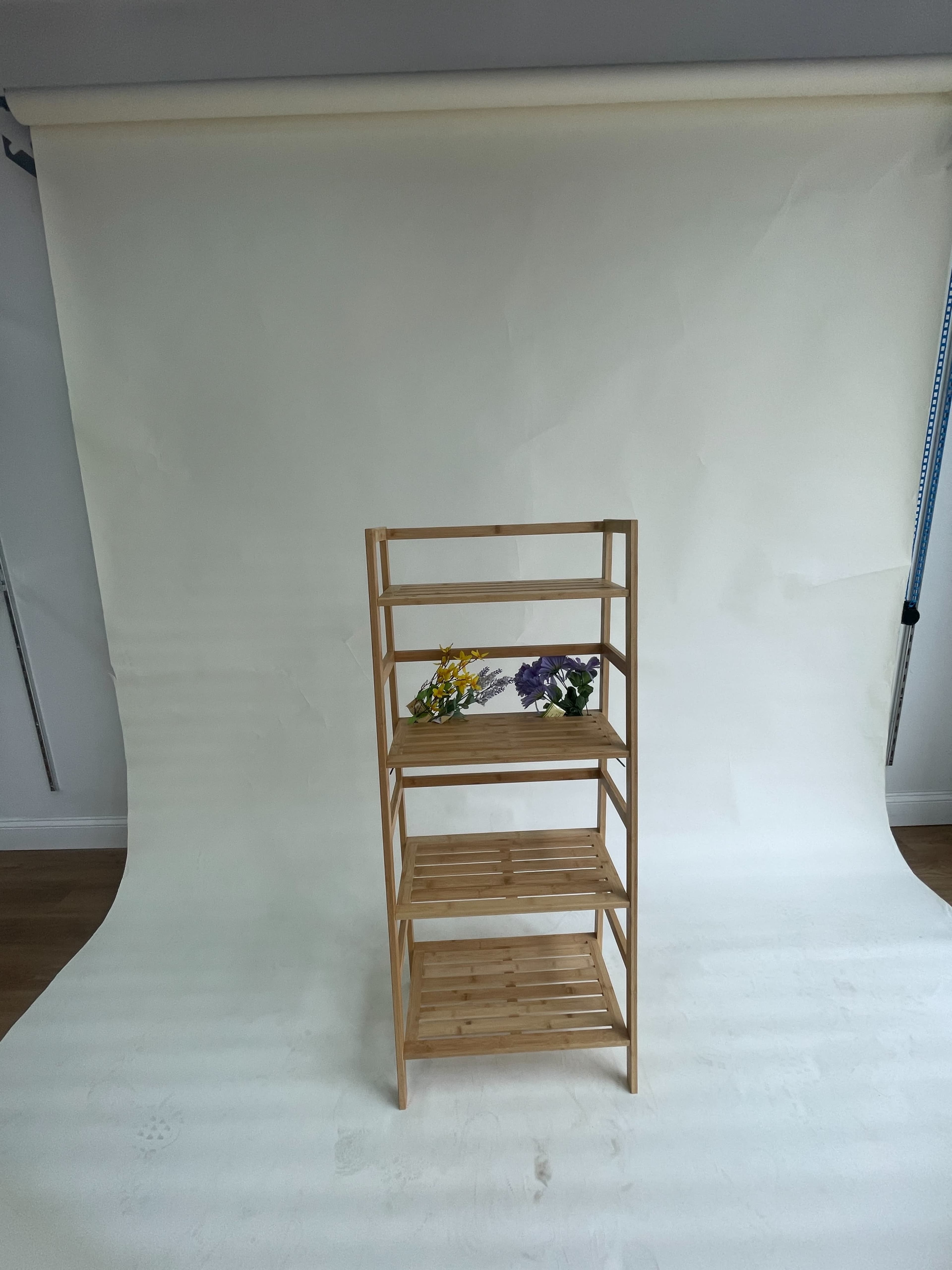 A wooden shelving unit with five shelves is positioned in front of a plain white backdrop, adorned with small flower arrangements on the top two shelves.