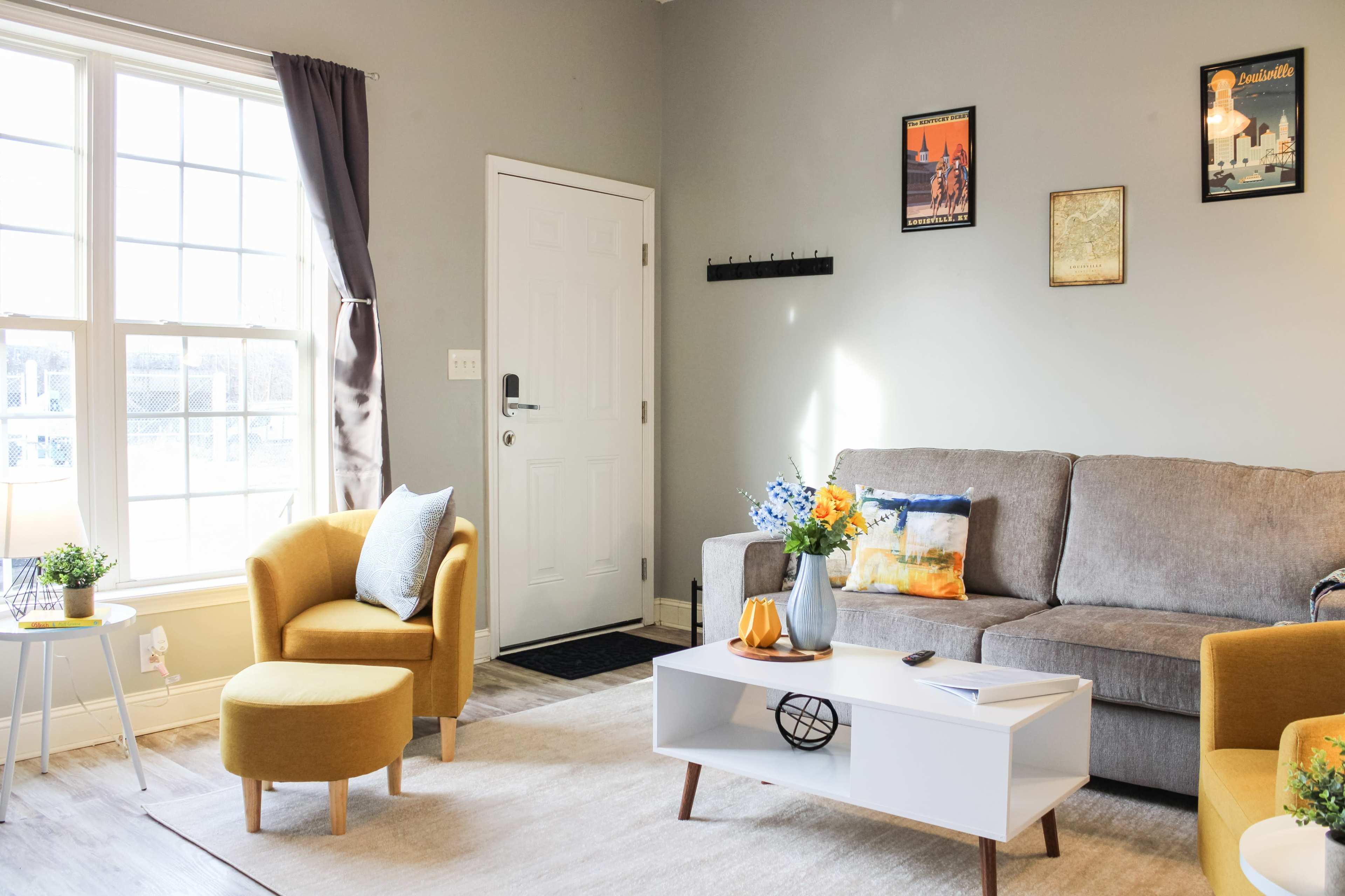 A living room with a gray sofa, a white coffee table, yellow armchairs, and a large window letting in natural light.