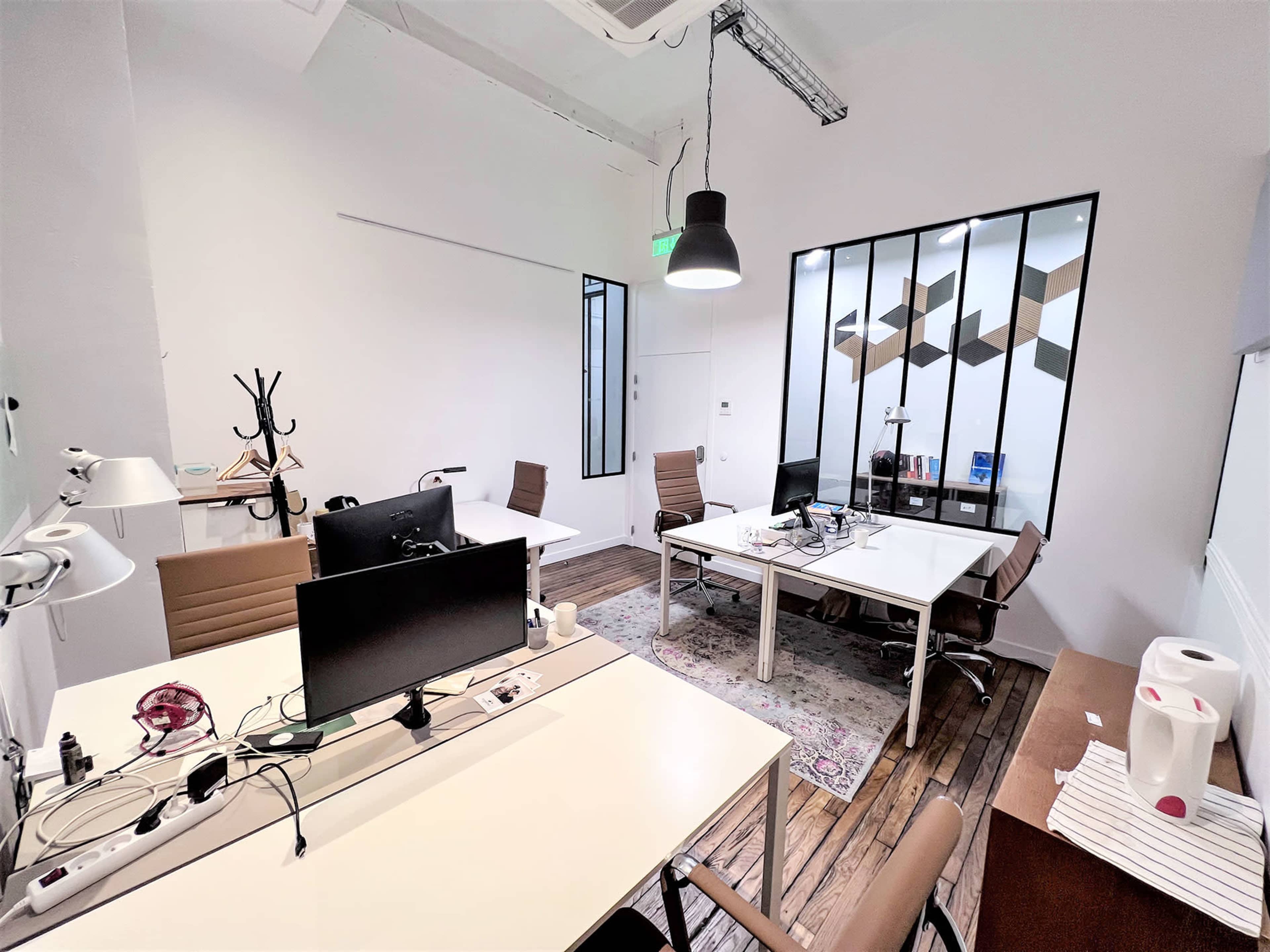 The image shows a modern office space with two distinct work areas featuring desks, chairs, and large windows, along with a brown cabinet in the corner.