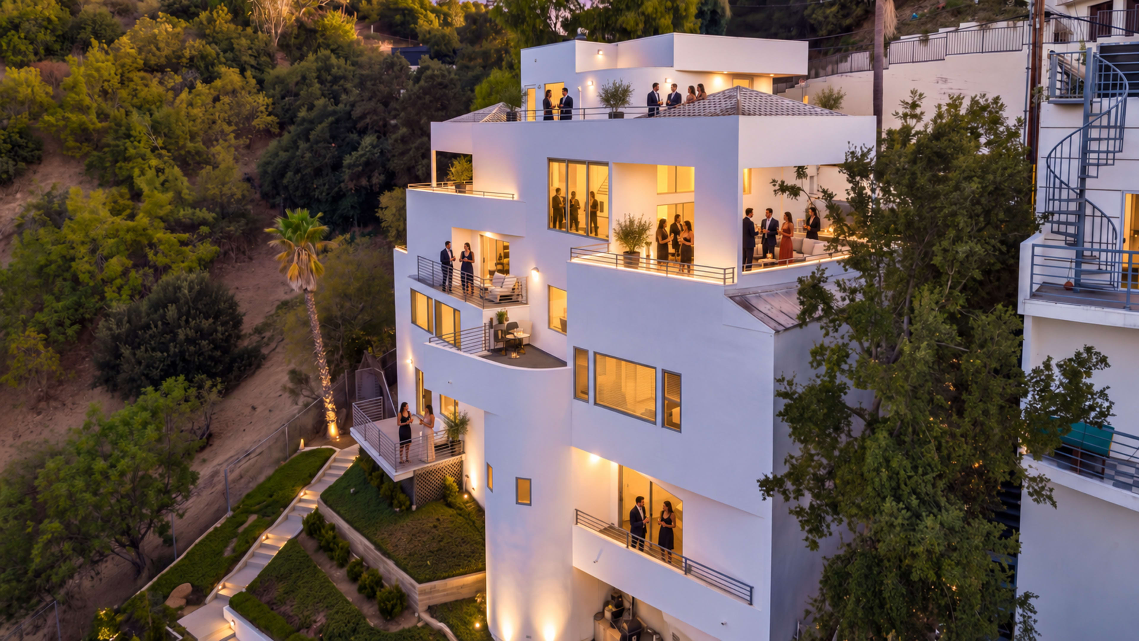 A modern three-story building with large windows and balconies is surrounded by greenery and features people socializing on its terraces during twilight.