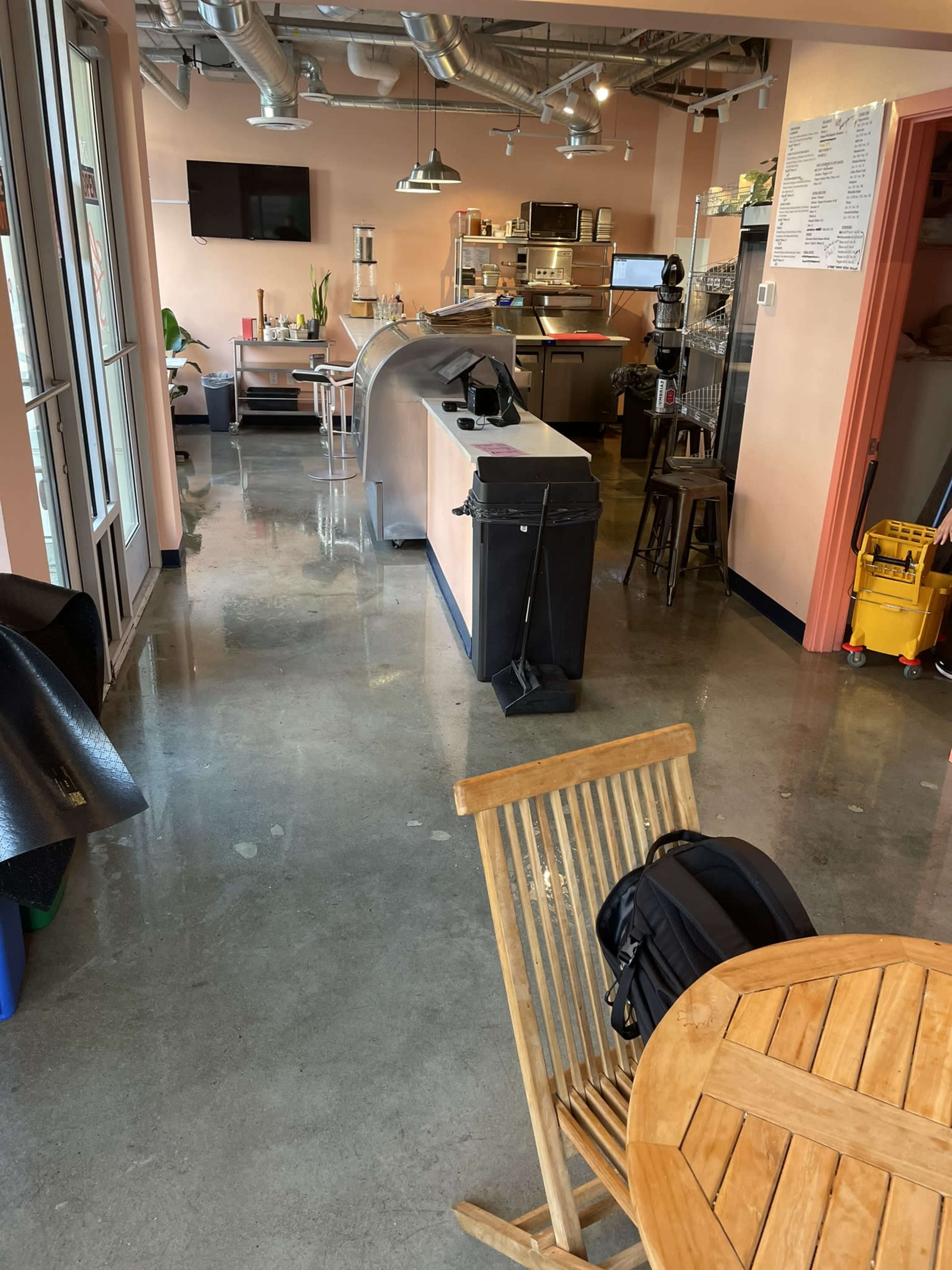 The image shows a clean, modern café interior with polished concrete floors, a service counter, and various kitchen equipment in the background.