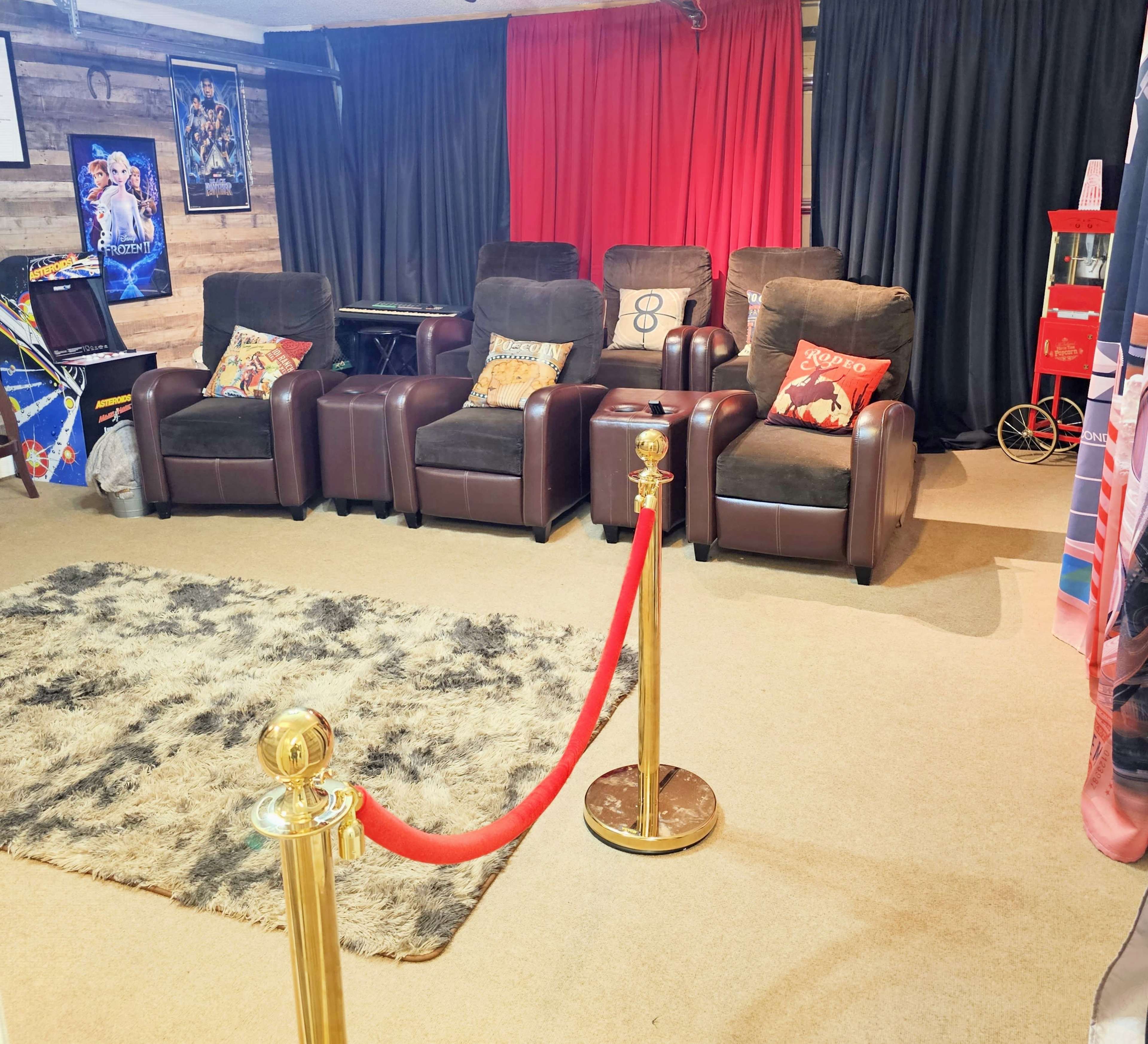 A home theater setup with brown reclining chairs, a red carpet, a movie-poster wall, and a popcorn machine.