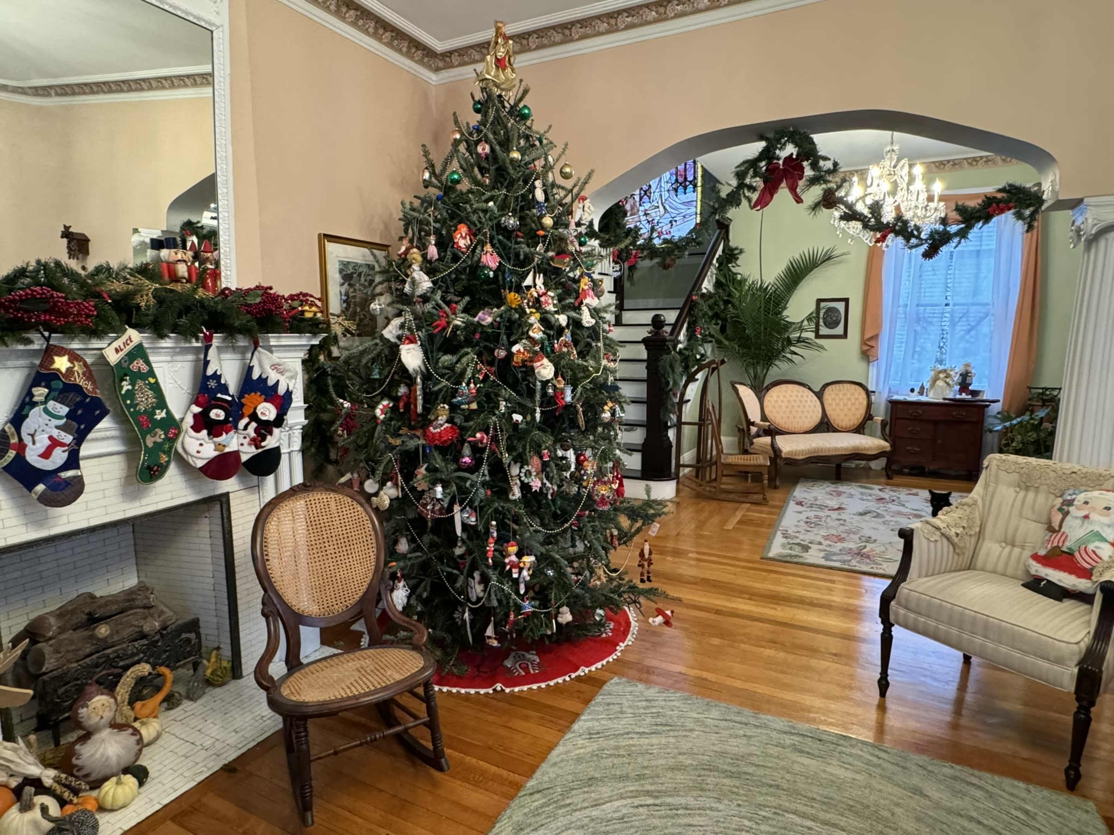 The living room features a decorated Christmas tree near a fireplace, surrounded by festive decorations and wooden furniture.