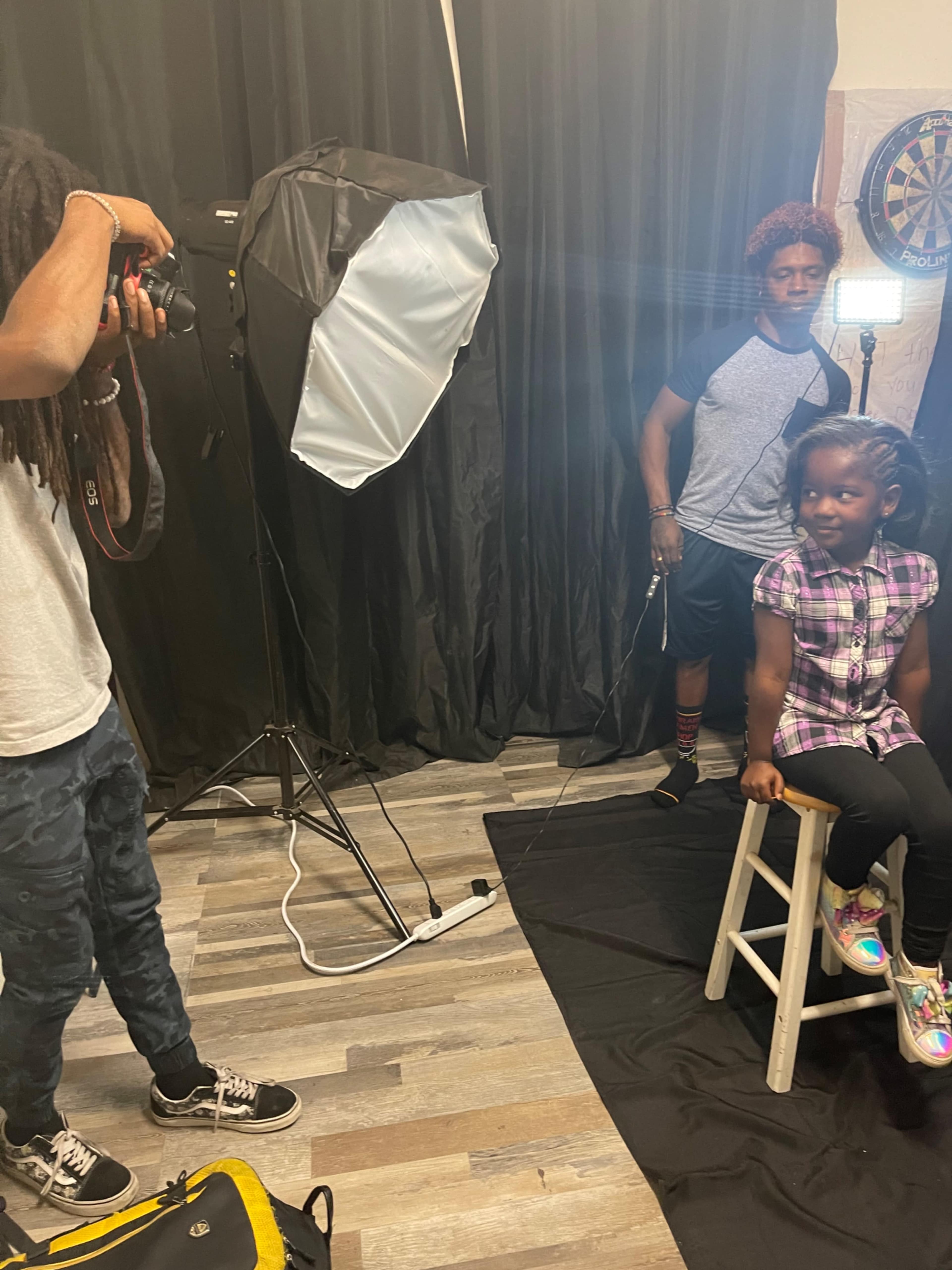 A photographer captures an image of a young girl sitting on a stool in a studio setting with professional lighting.
