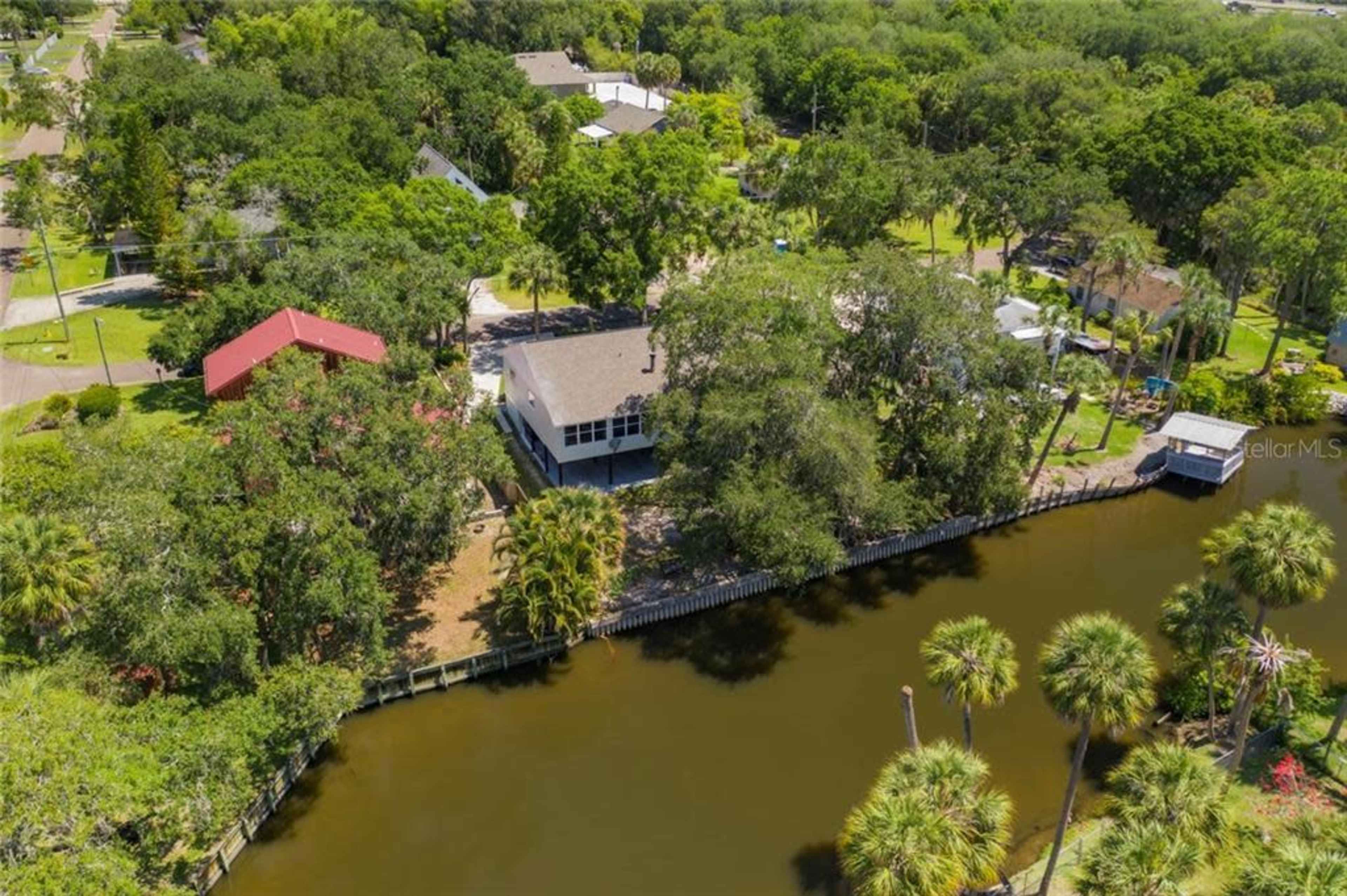 An aerial view of a residential area with a canal, surrounded by trees and several houses, including one with a red roof.