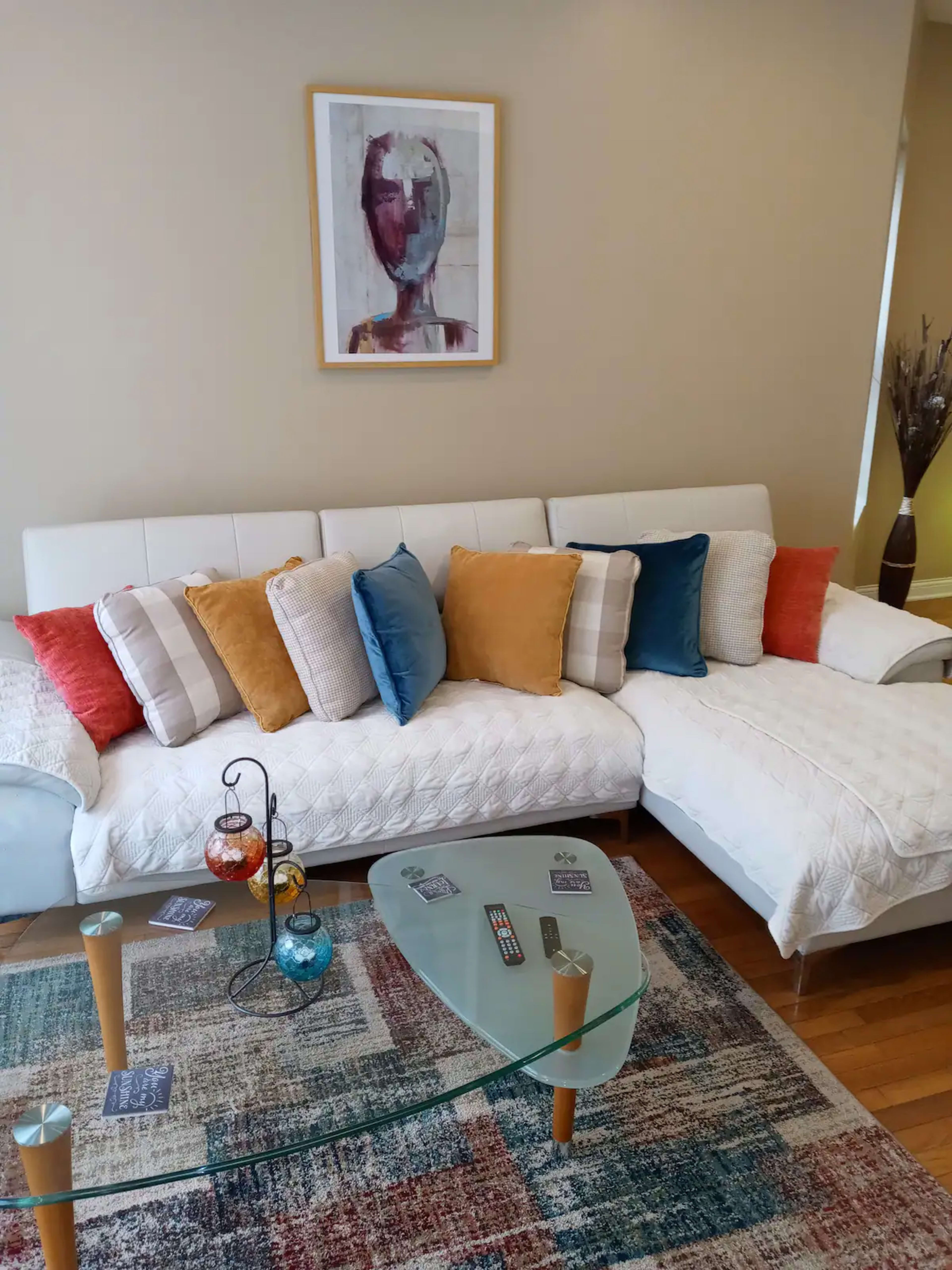 A modern living room with a sectional sofa adorned with colorful cushions, a glass coffee table, and a decorative rug.