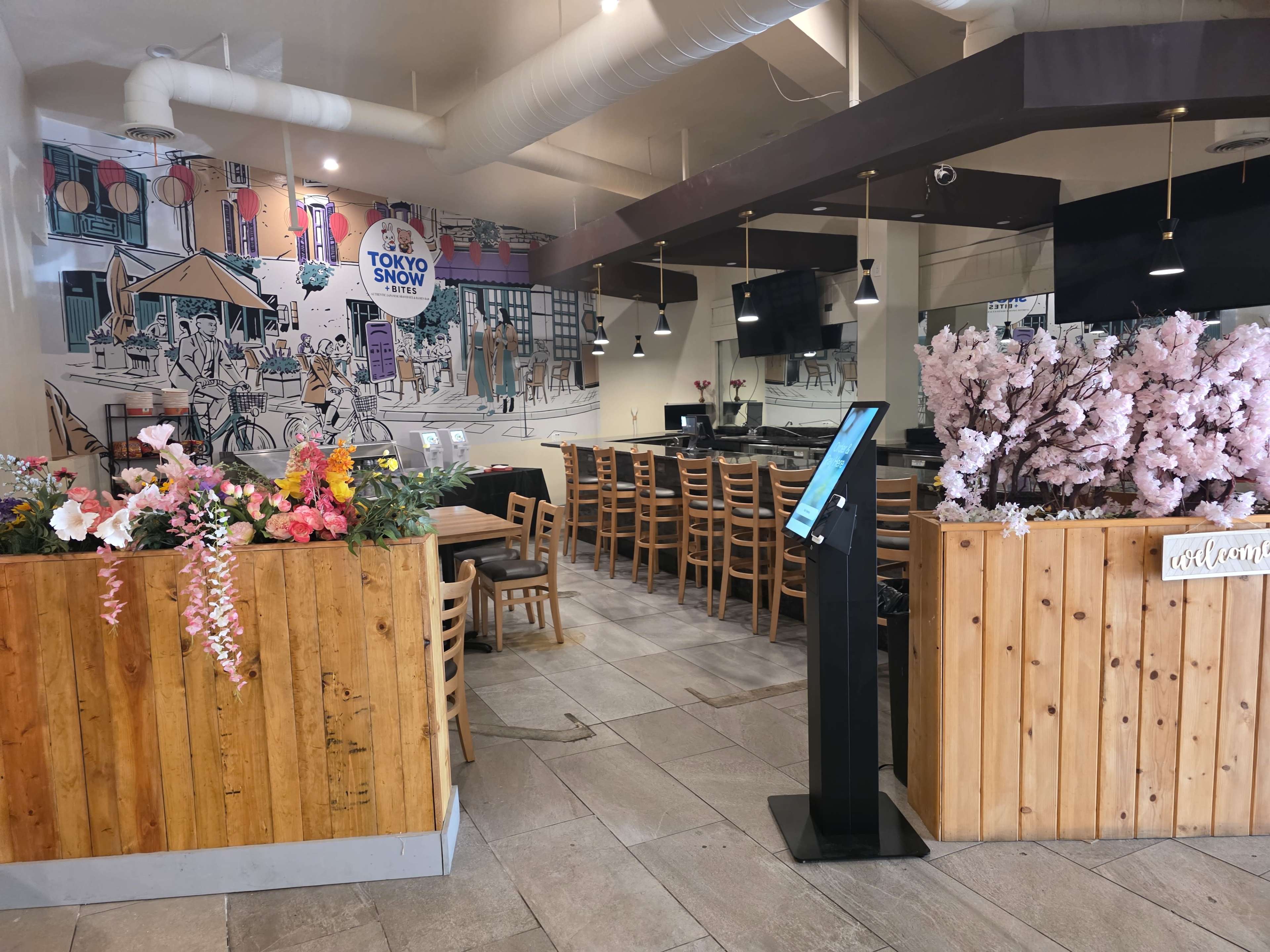 The image shows the interior of a restaurant featuring wooden furniture, floral decorations, and an illustrated mural on the wall.