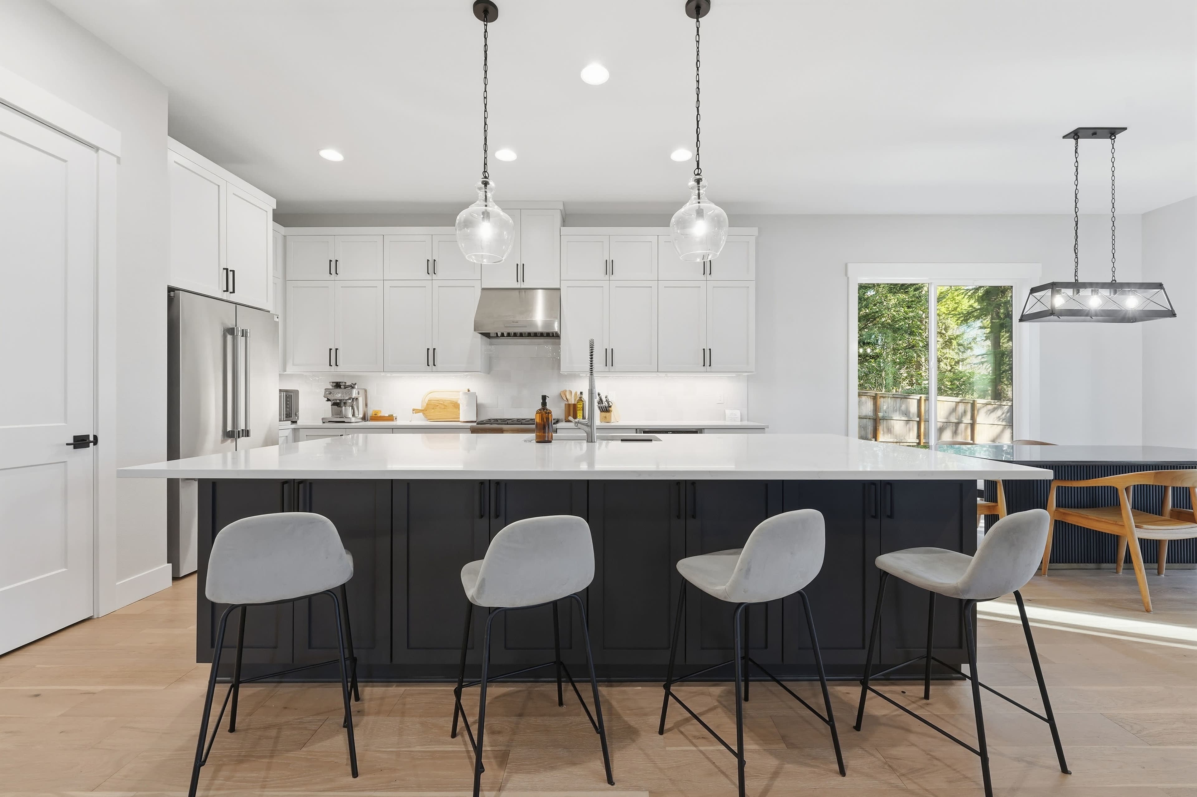A modern kitchen features white cabinetry, stainless steel appliances, a large island with bar stools, and a dining area with a table and chairs.