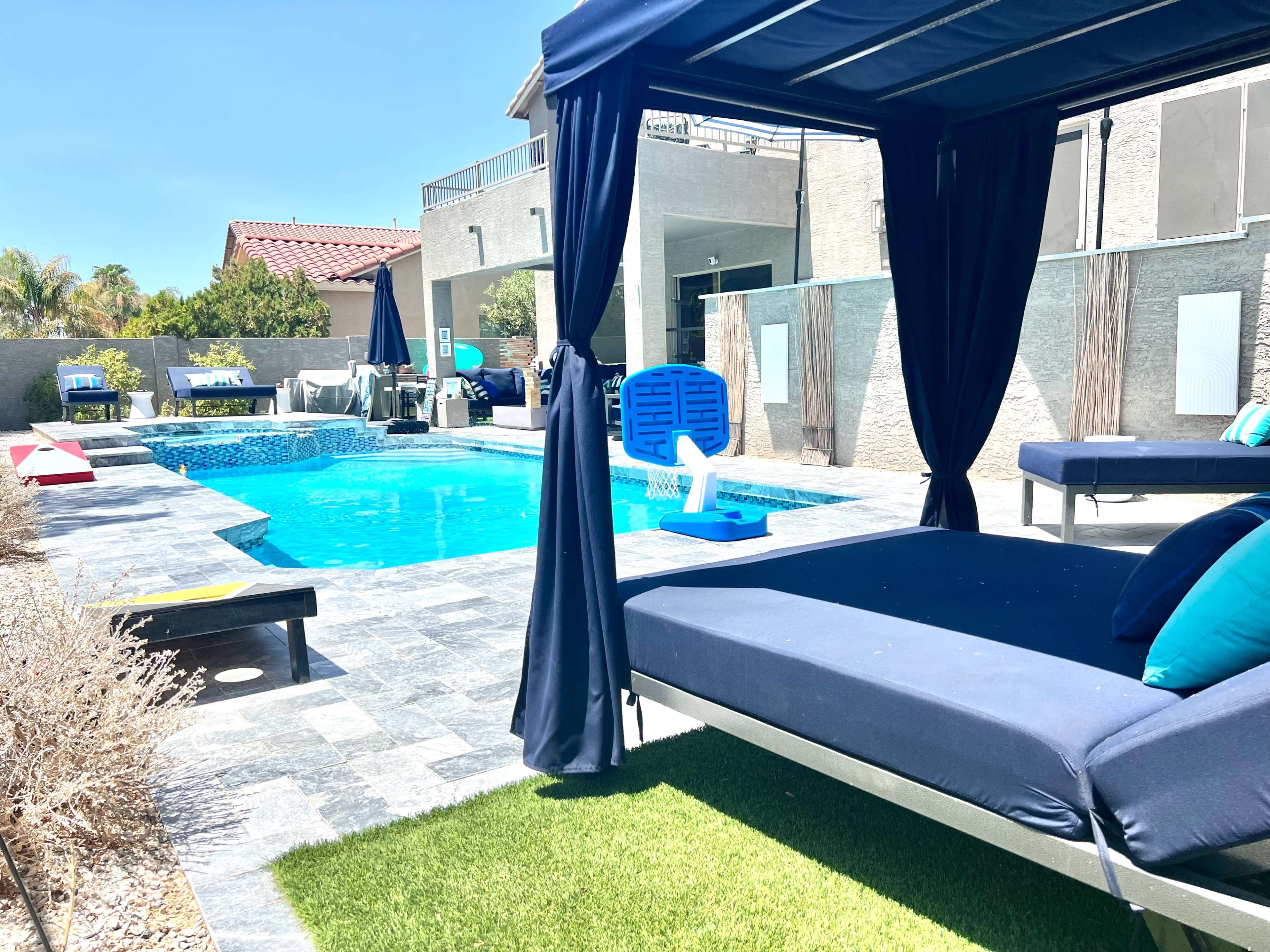The image shows a modern outdoor pool area with a blue pool, lounge chairs, and a shaded seating area.