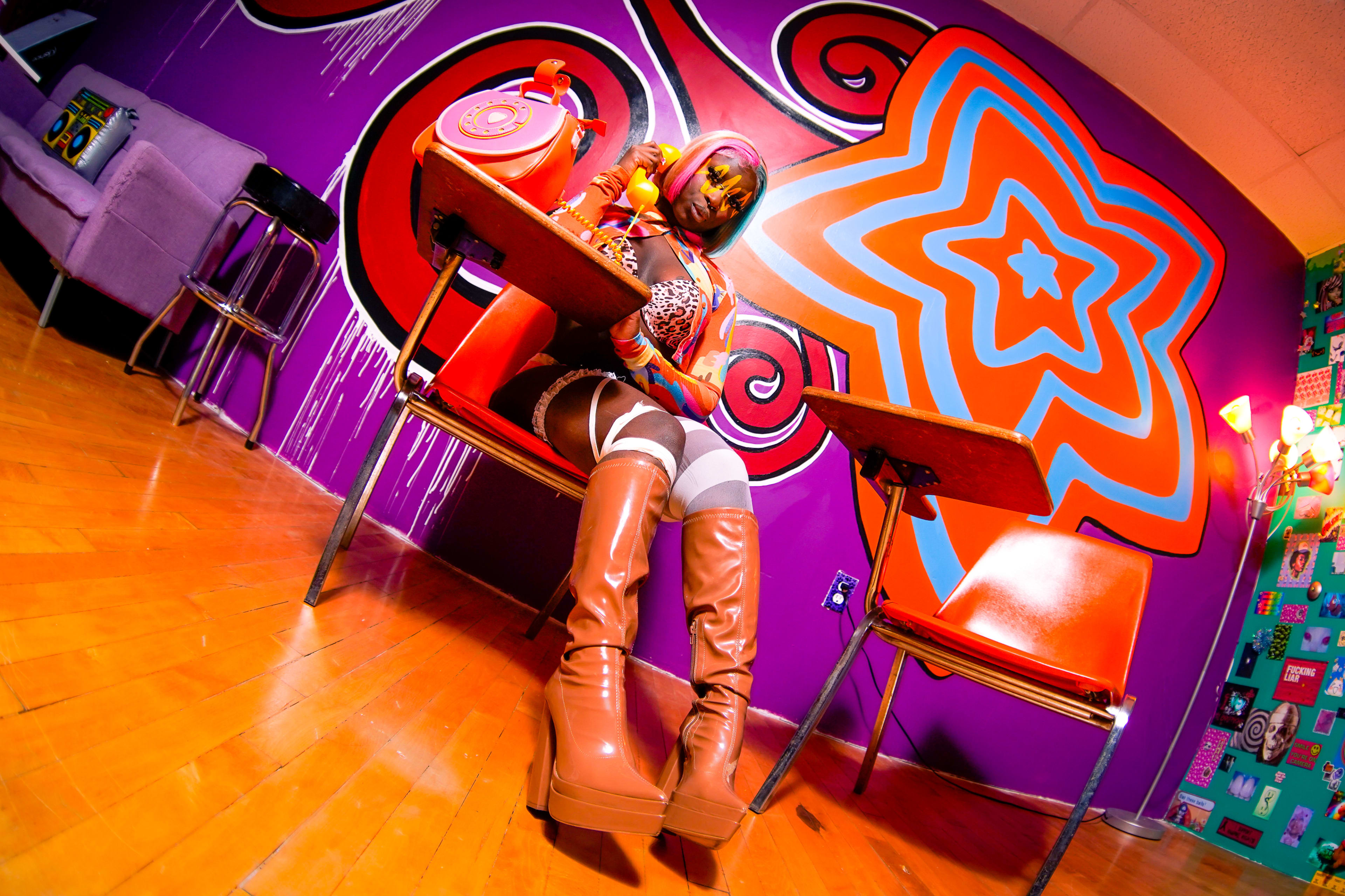 A person sits at a retro-style desk in a brightly colored room with abstract wall designs and furniture.
