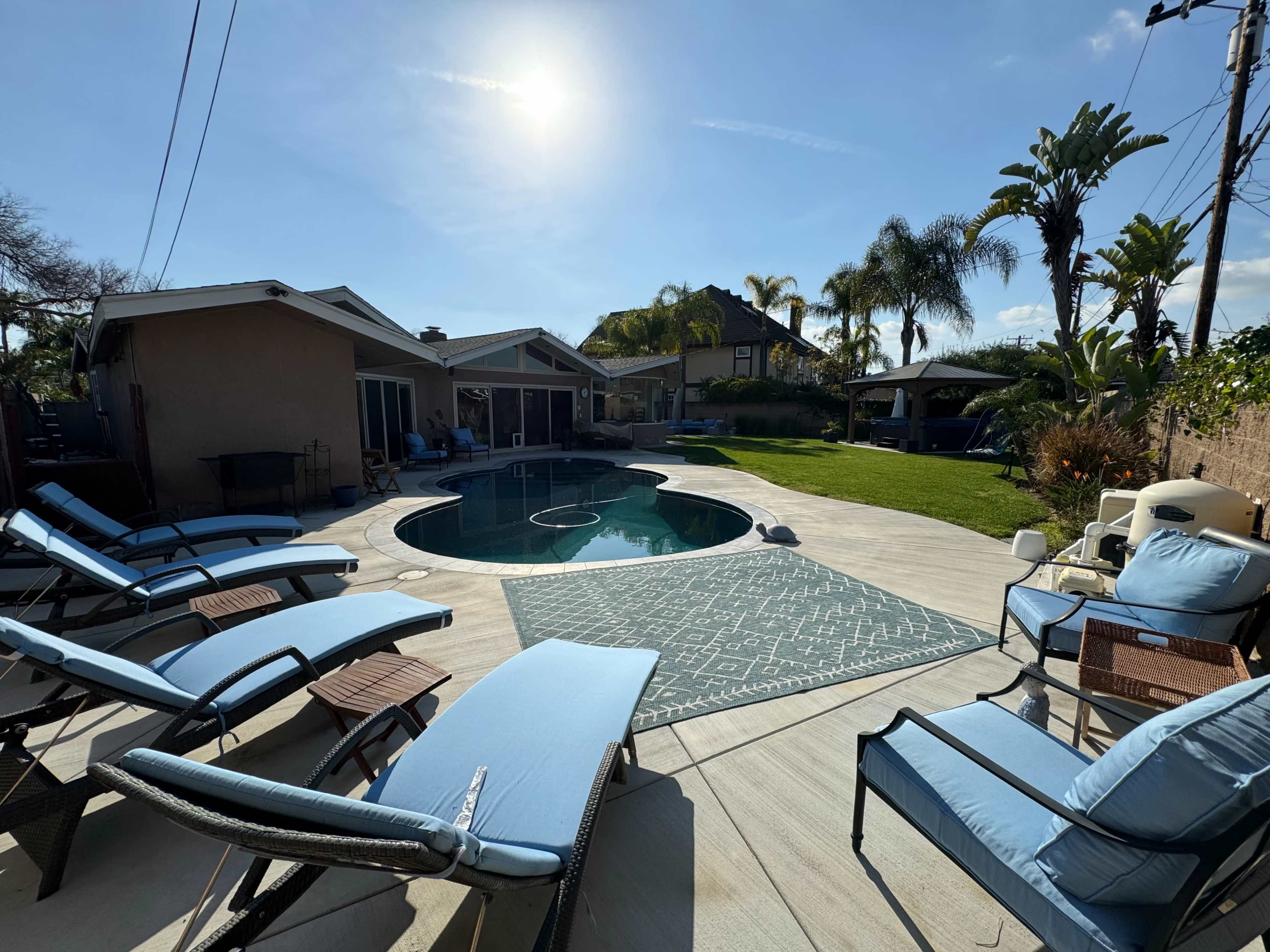 A pool area with lounge chairs, a circular pool, and surrounding landscaped lawn and palm trees under a clear sky.