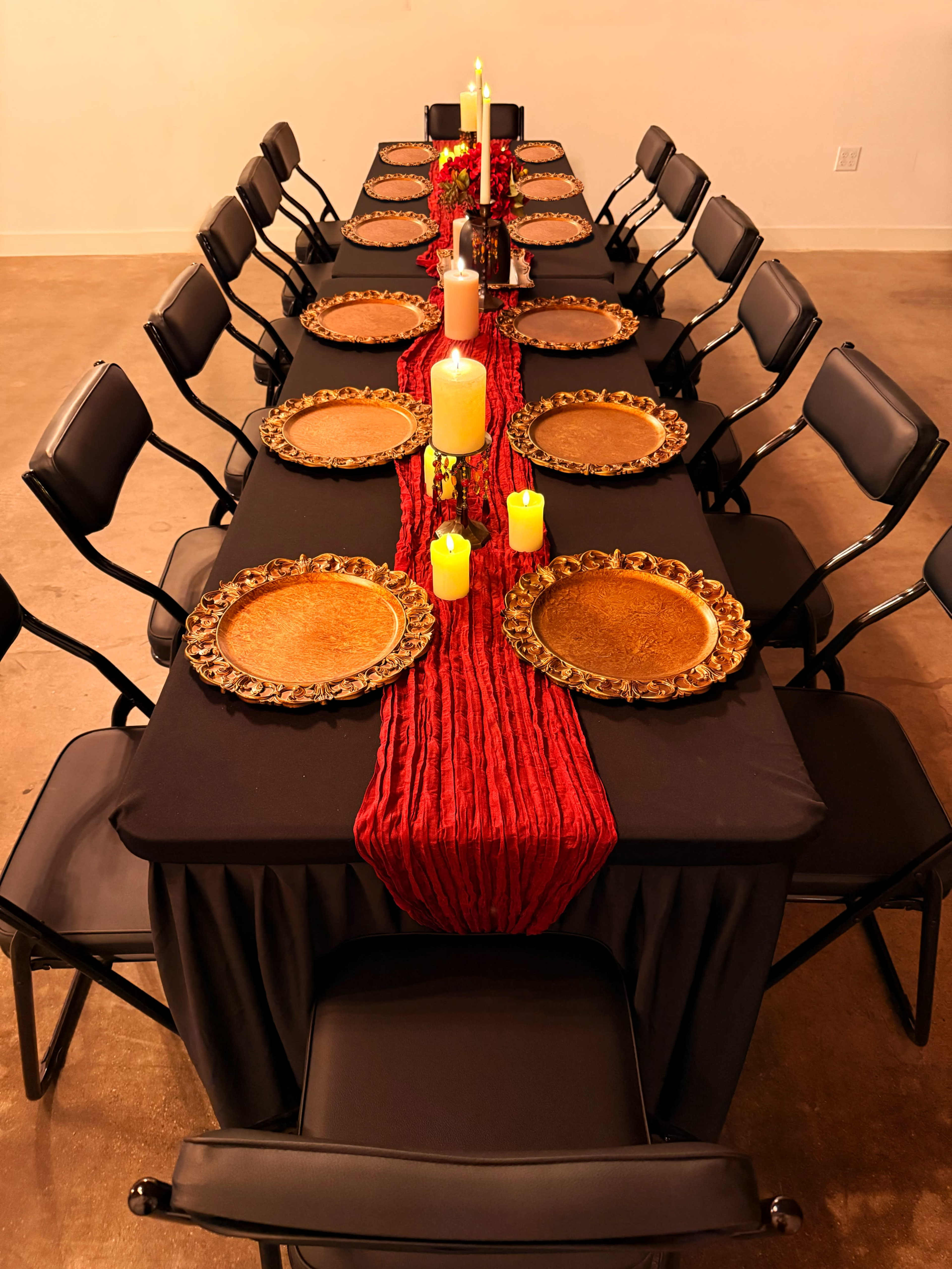 A long banquet table is set with black tablecloths, golden plates, and candles arranged along a red runner.
