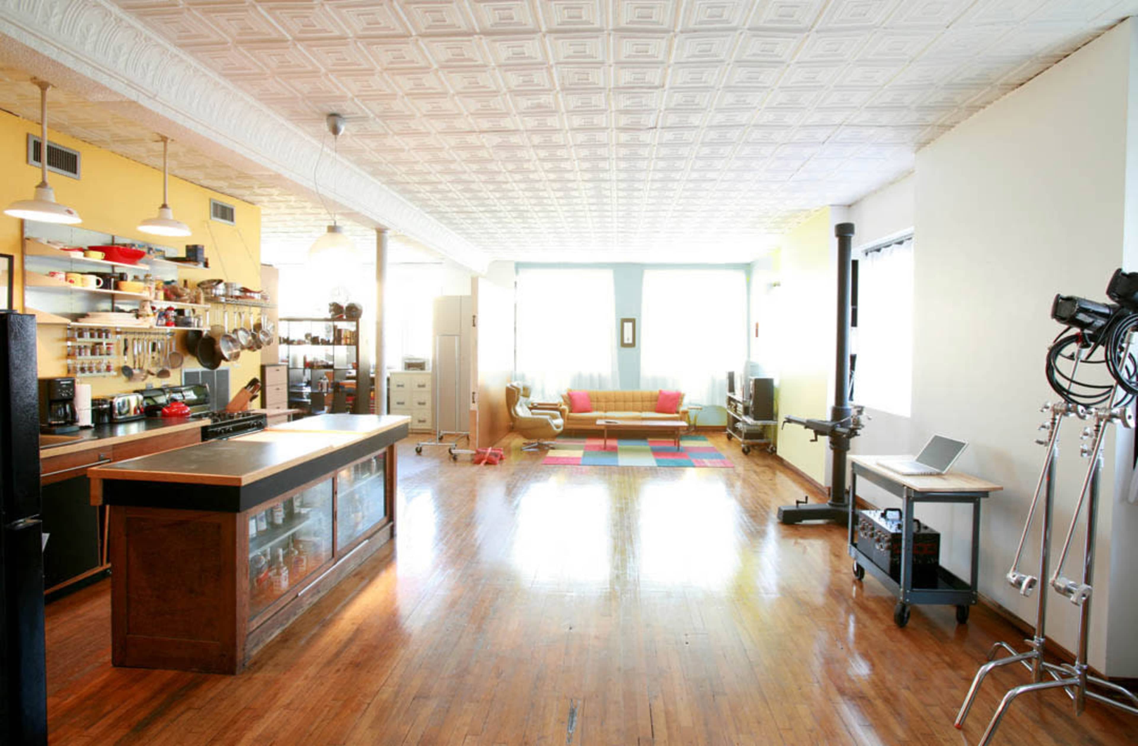 A spacious, bright room featuring a kitchen area with a counter, a cozy seating area with a sofa, and a colorful rug on the wooden floor.