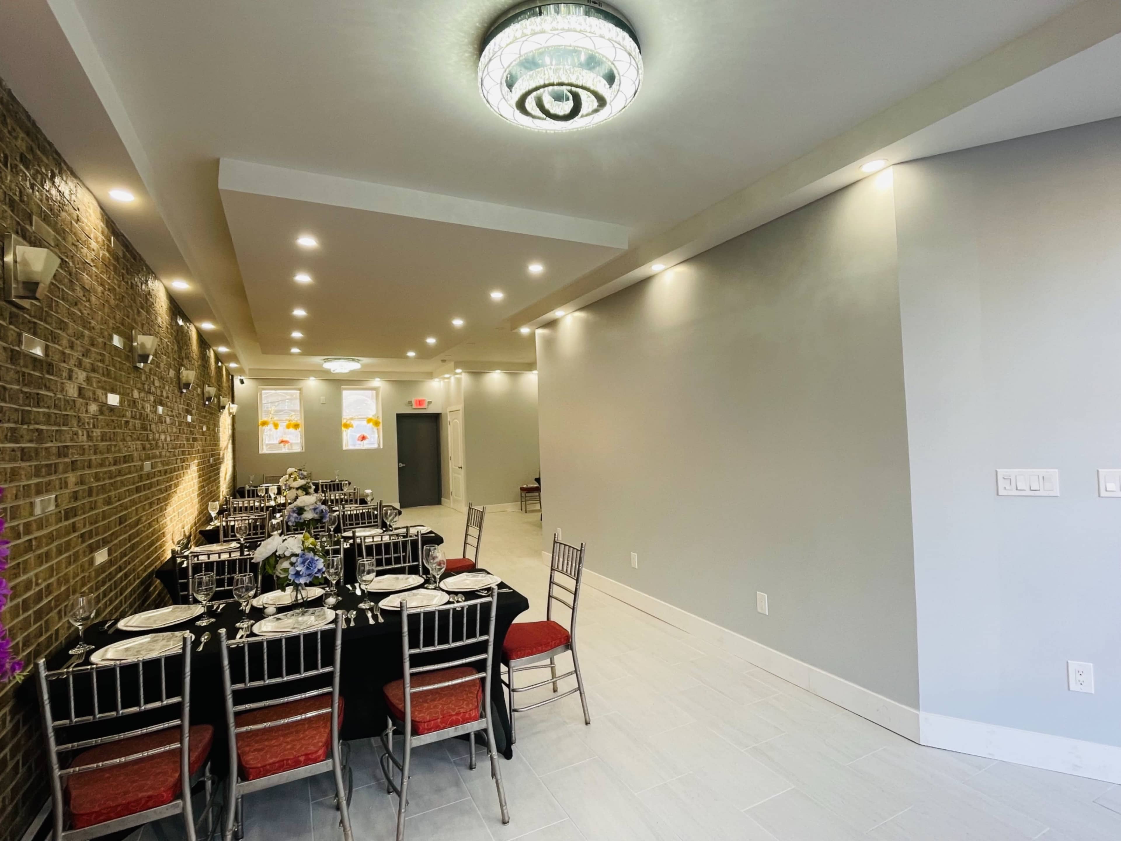 A long dining area with a black tablecloth set for a meal, flanked by chairs, and illuminated by overhead lights.