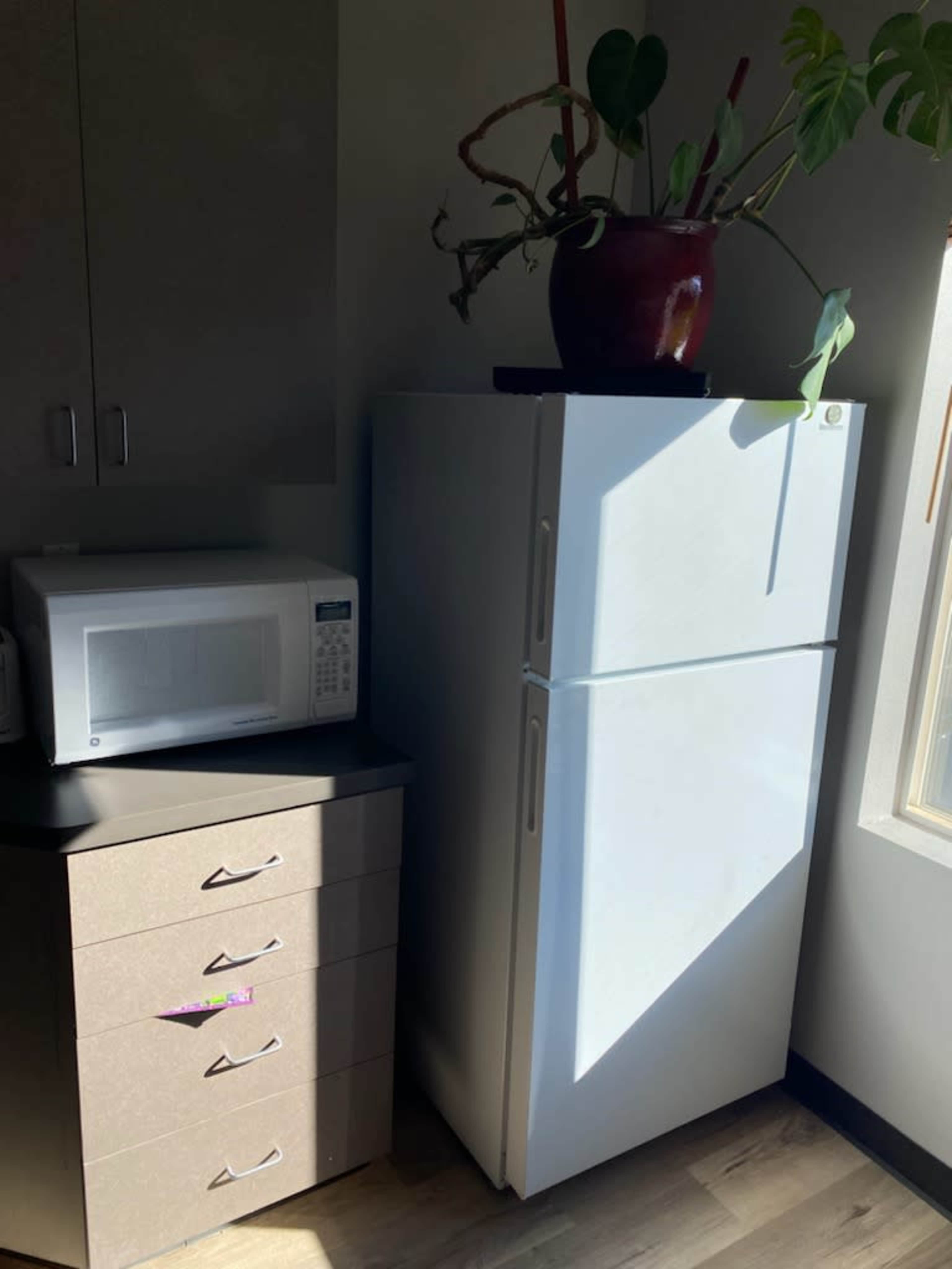 A white refrigerator next to a microwave and a set of drawers in a well-lit corner of a room.
