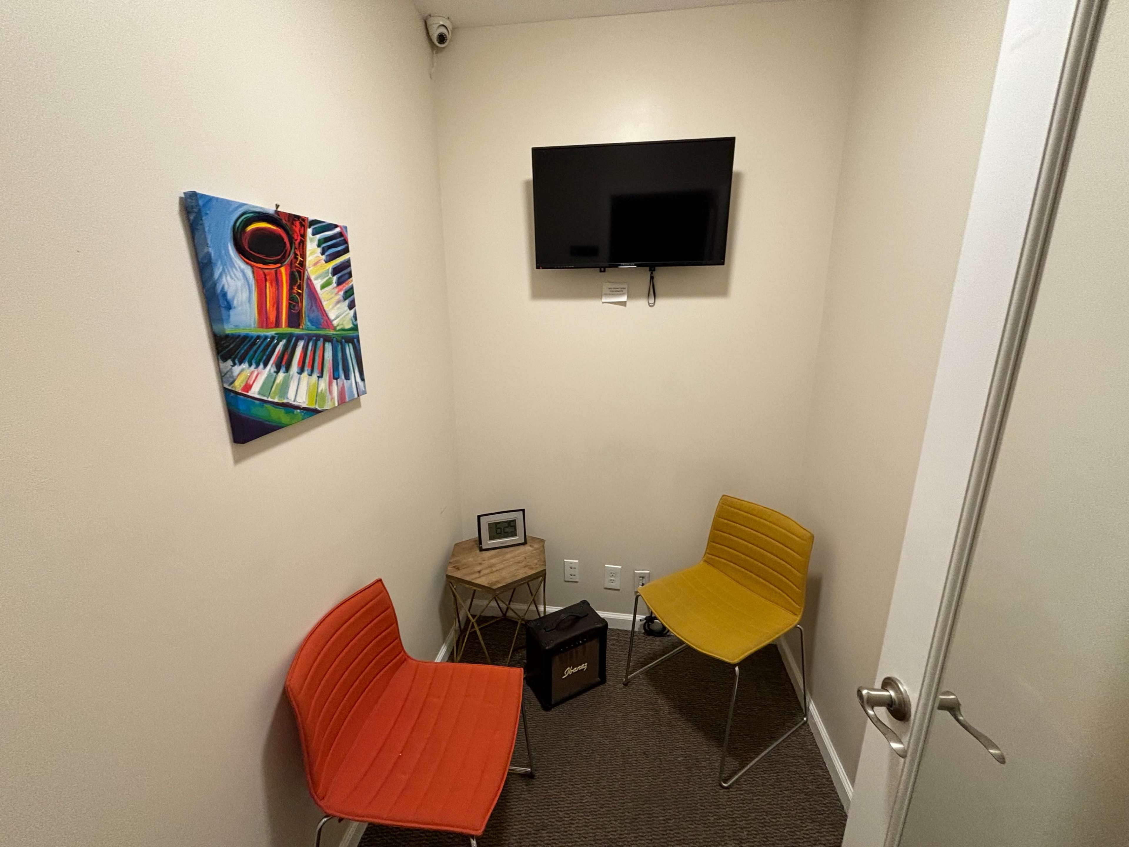 A small room with two colored chairs, a television mounted on the wall, a piece of artwork, and a small table.