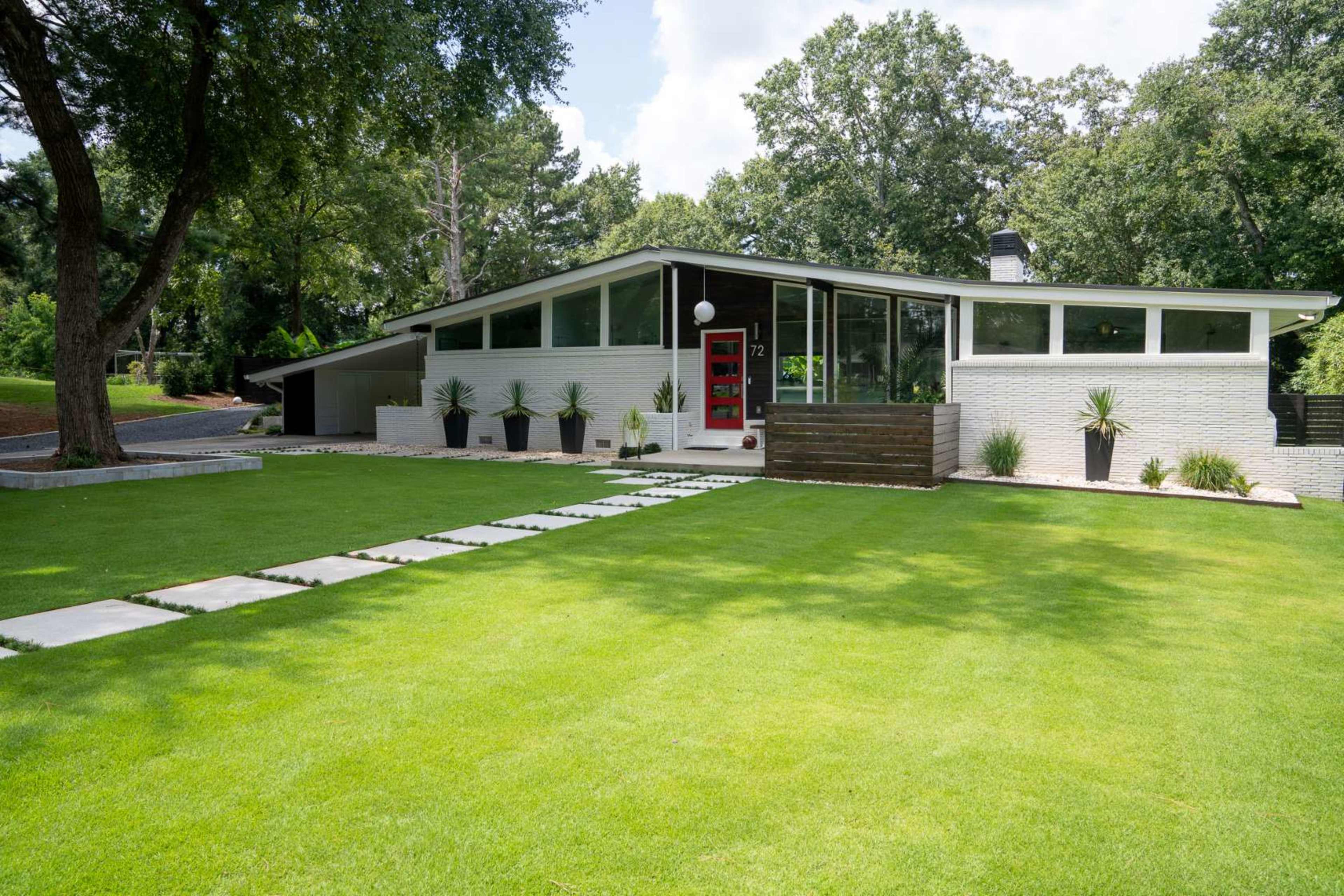 A modern house with a flat roof, large windows, and a red front door, surrounded by a well-maintained lawn and stone pathway.