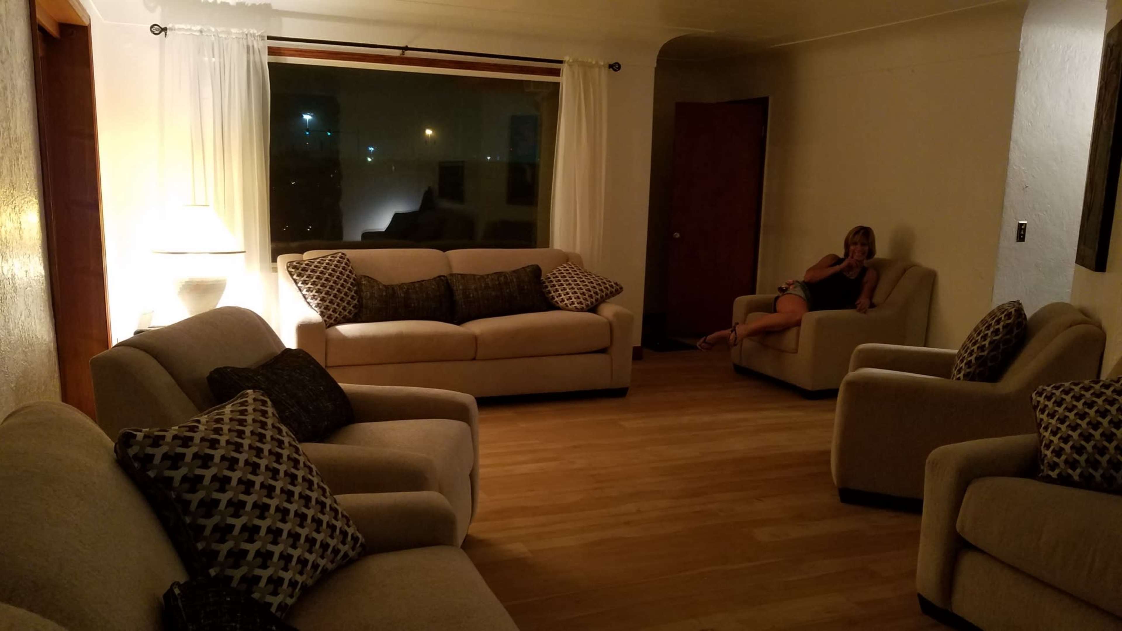 A living room with four light-colored sofas arranged around a wooden floor, accompanied by a woman sitting on one of the sofas.