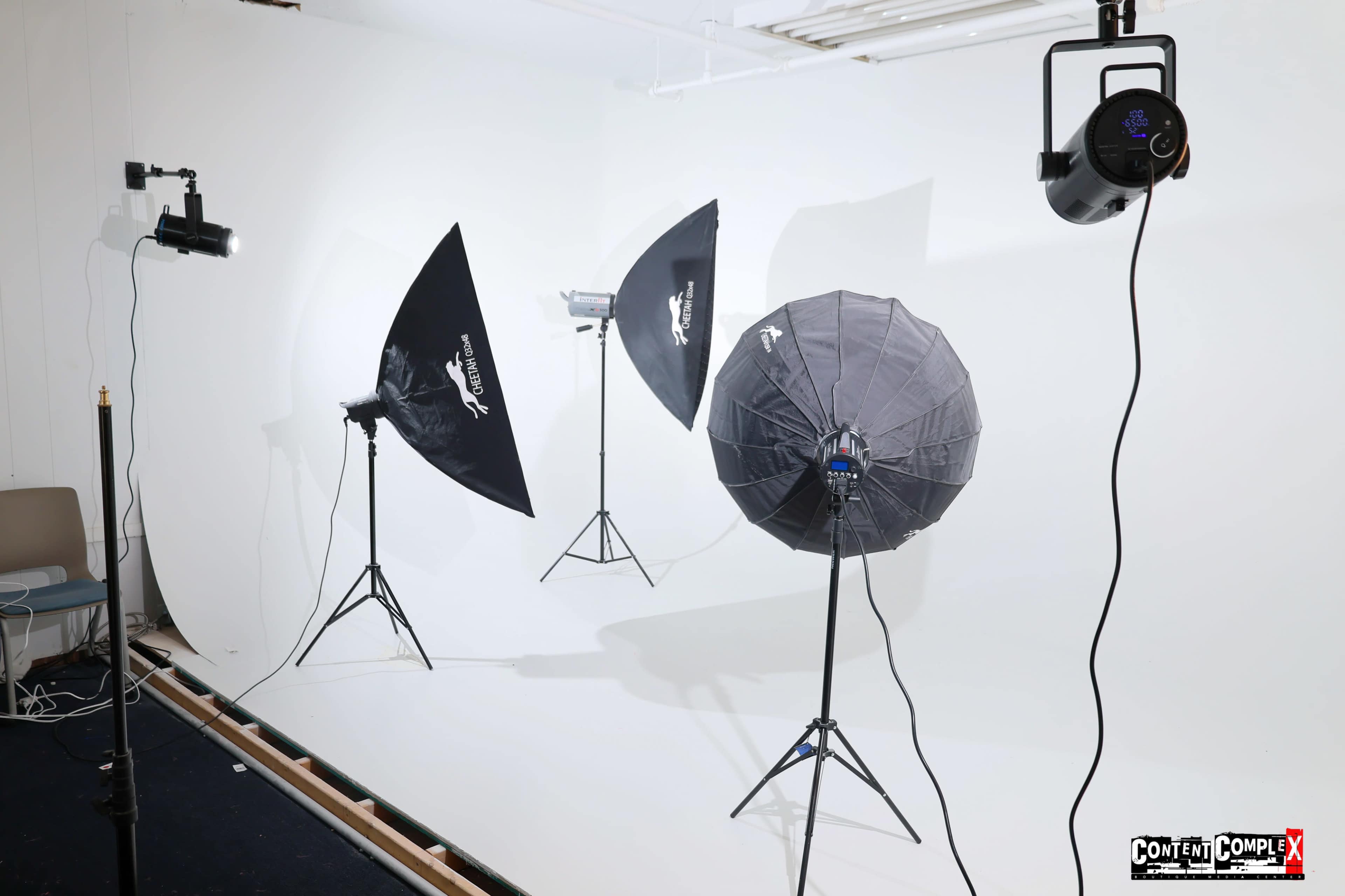 A photography studio setup with various softbox lights and an umbrella reflector on a white backdrop.