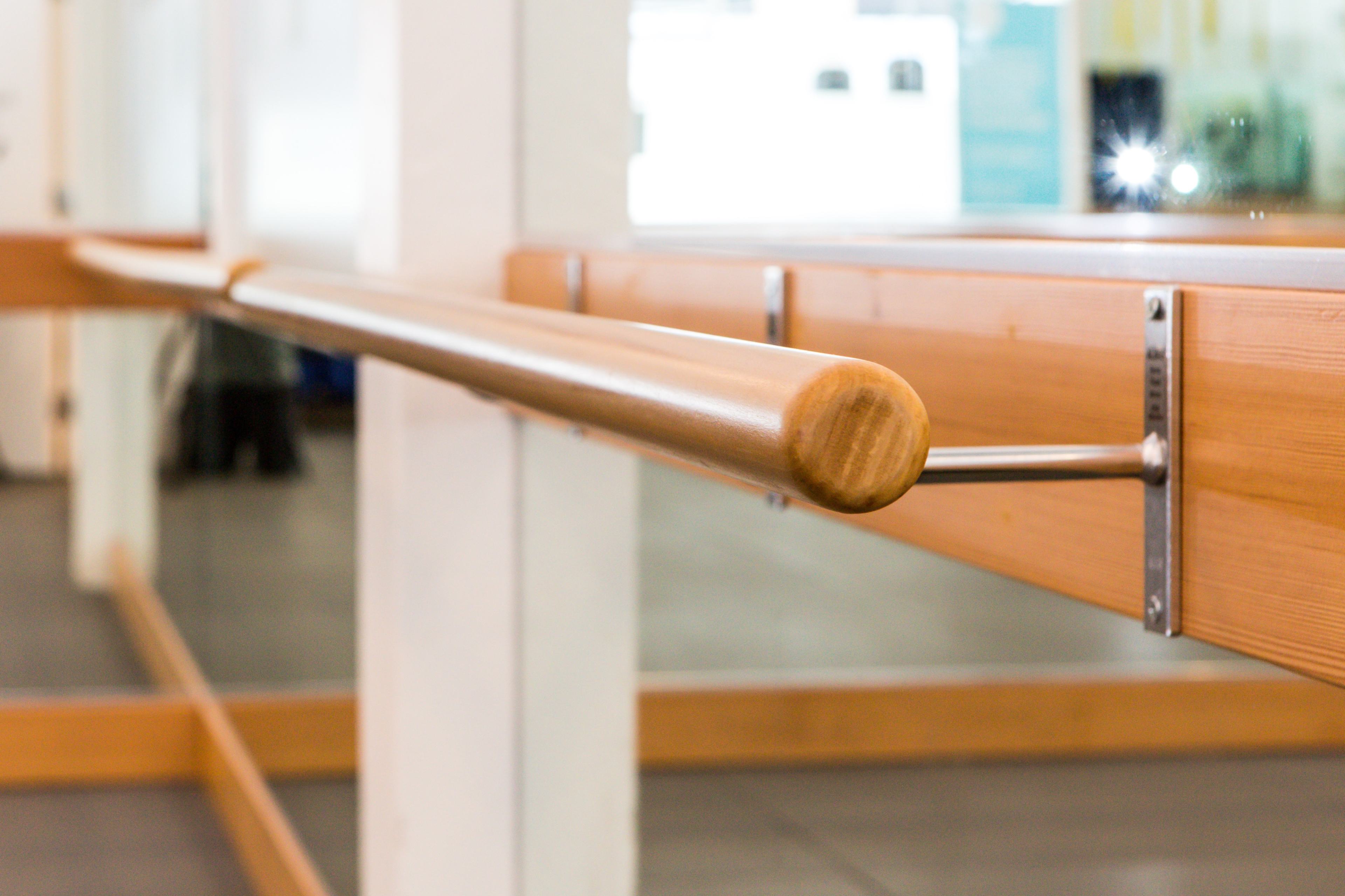 A wooden ballet barre attached to a wall in a studio with mirrors.