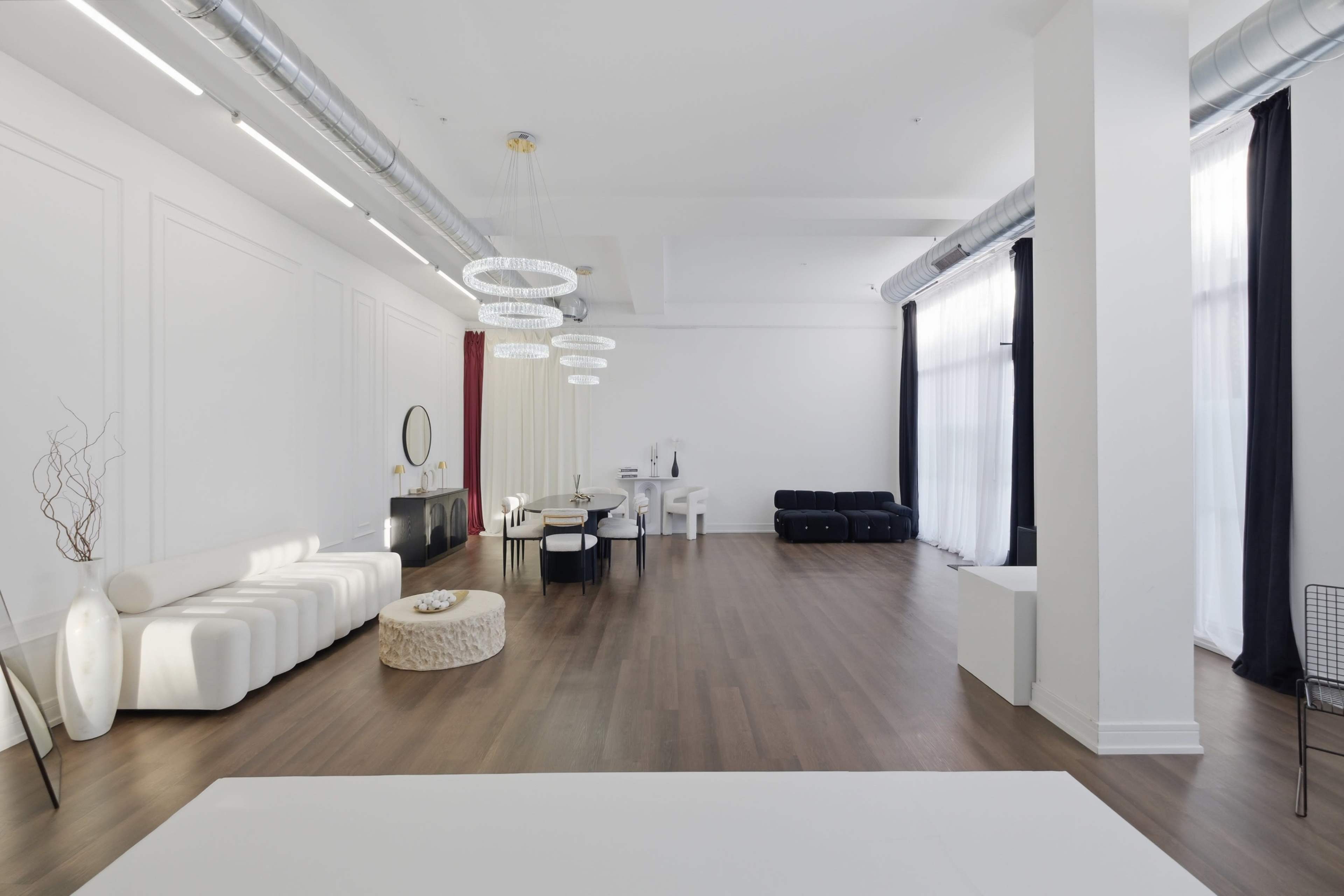 The image shows a spacious, well-lit interior with modern furniture, including a sectional sofa, dining table, and decorative accessories.