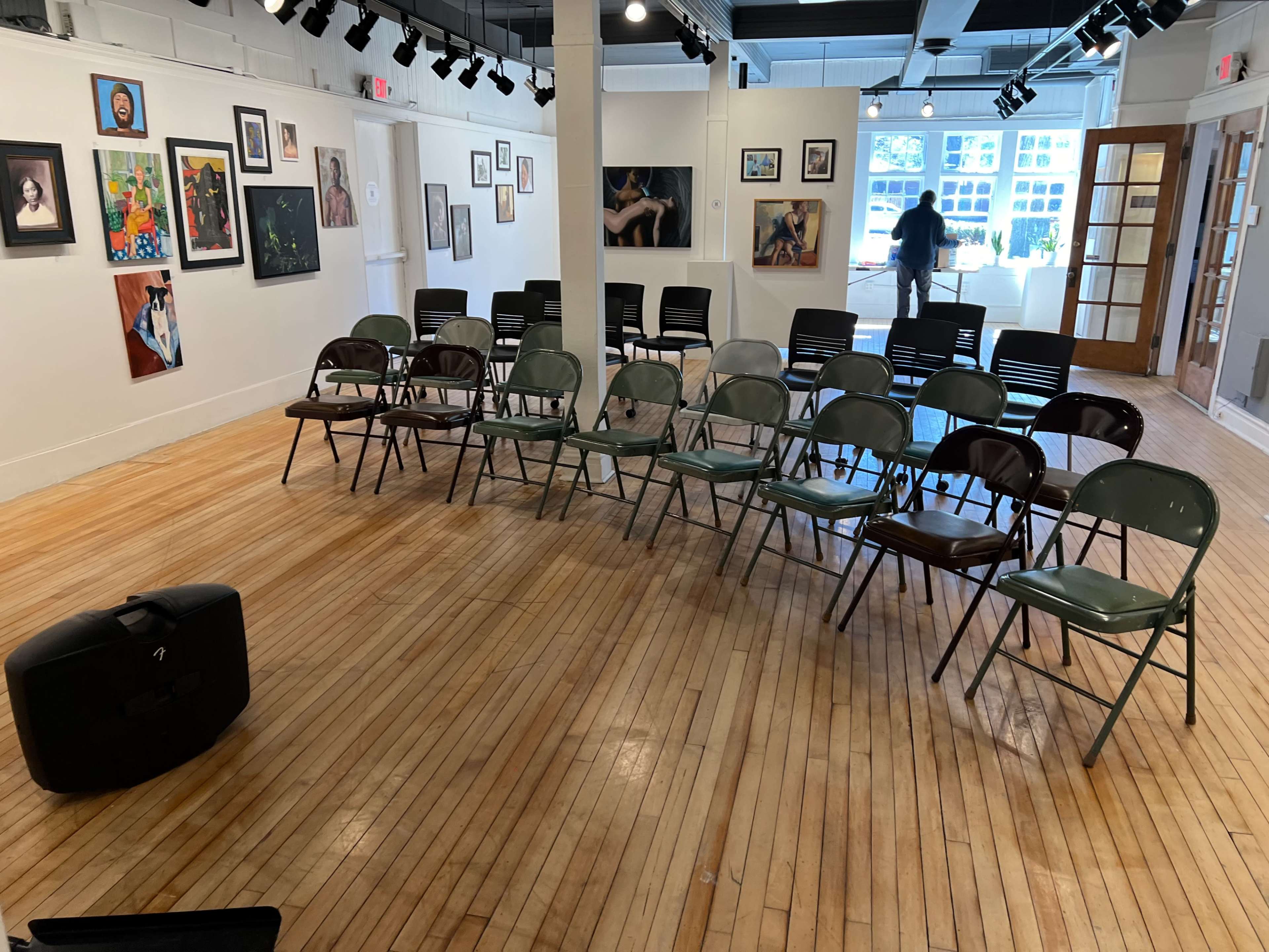 An art gallery features a semicircle of chairs arranged around a central area, with various artworks displayed on the walls.