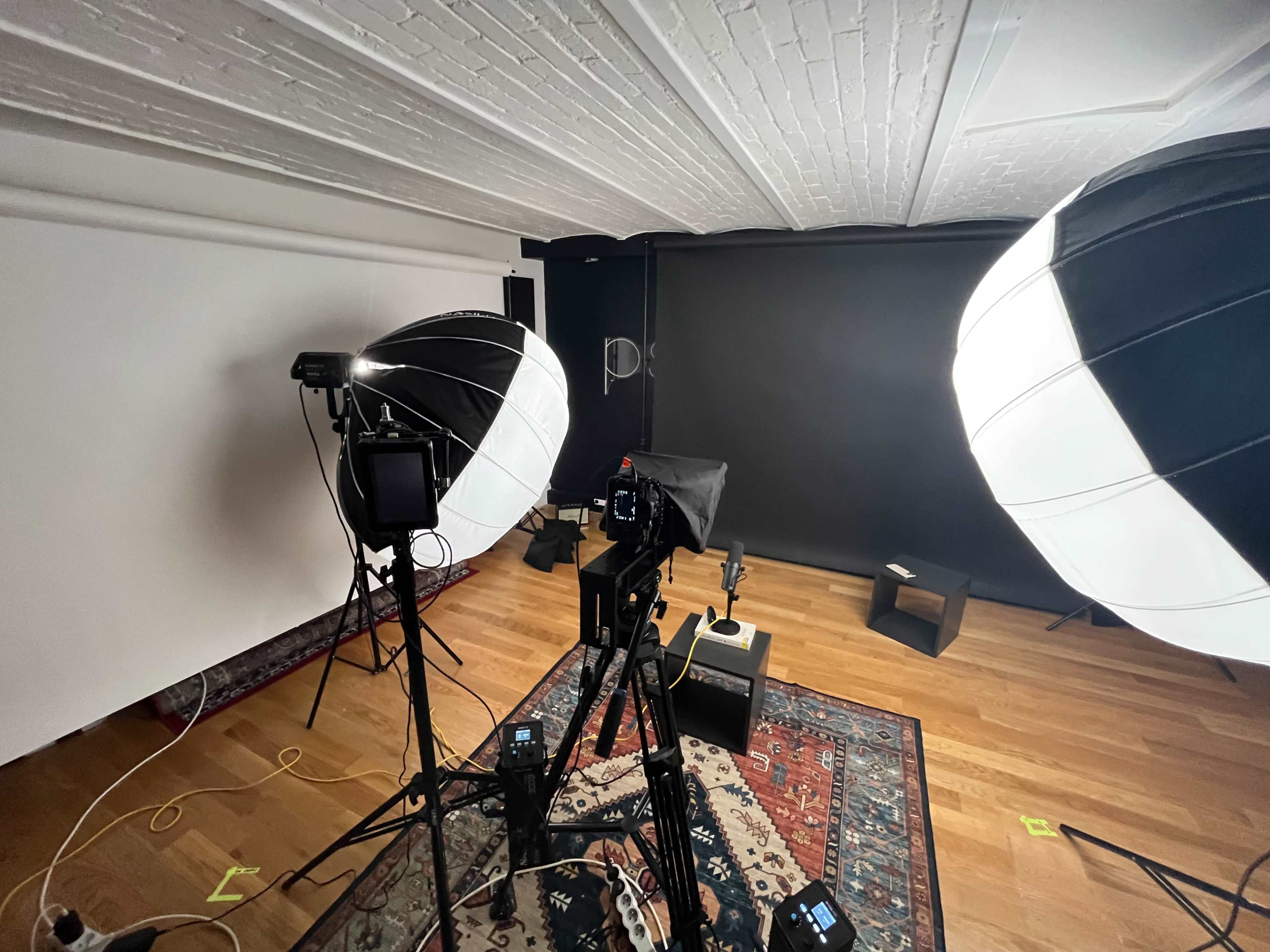 A photography studio setup with two large softbox lights, a camera on a tripod, and a dark backdrop, all placed on a wooden floor with a patterned rug.