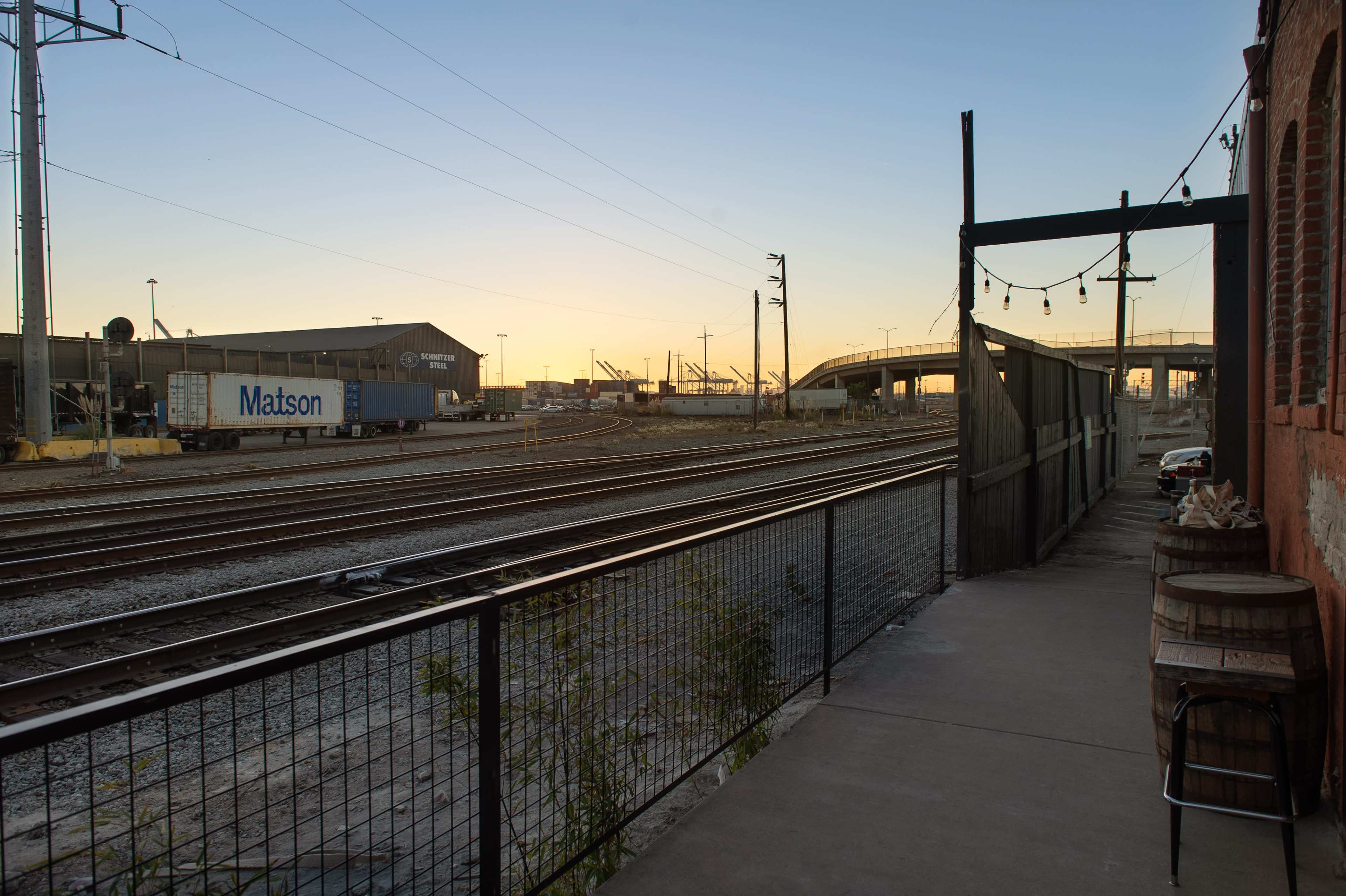 The scene shows a railway track alongside a walkway, with a shipping container labeled "Matson" and a distant sunset behind industrial buildings.