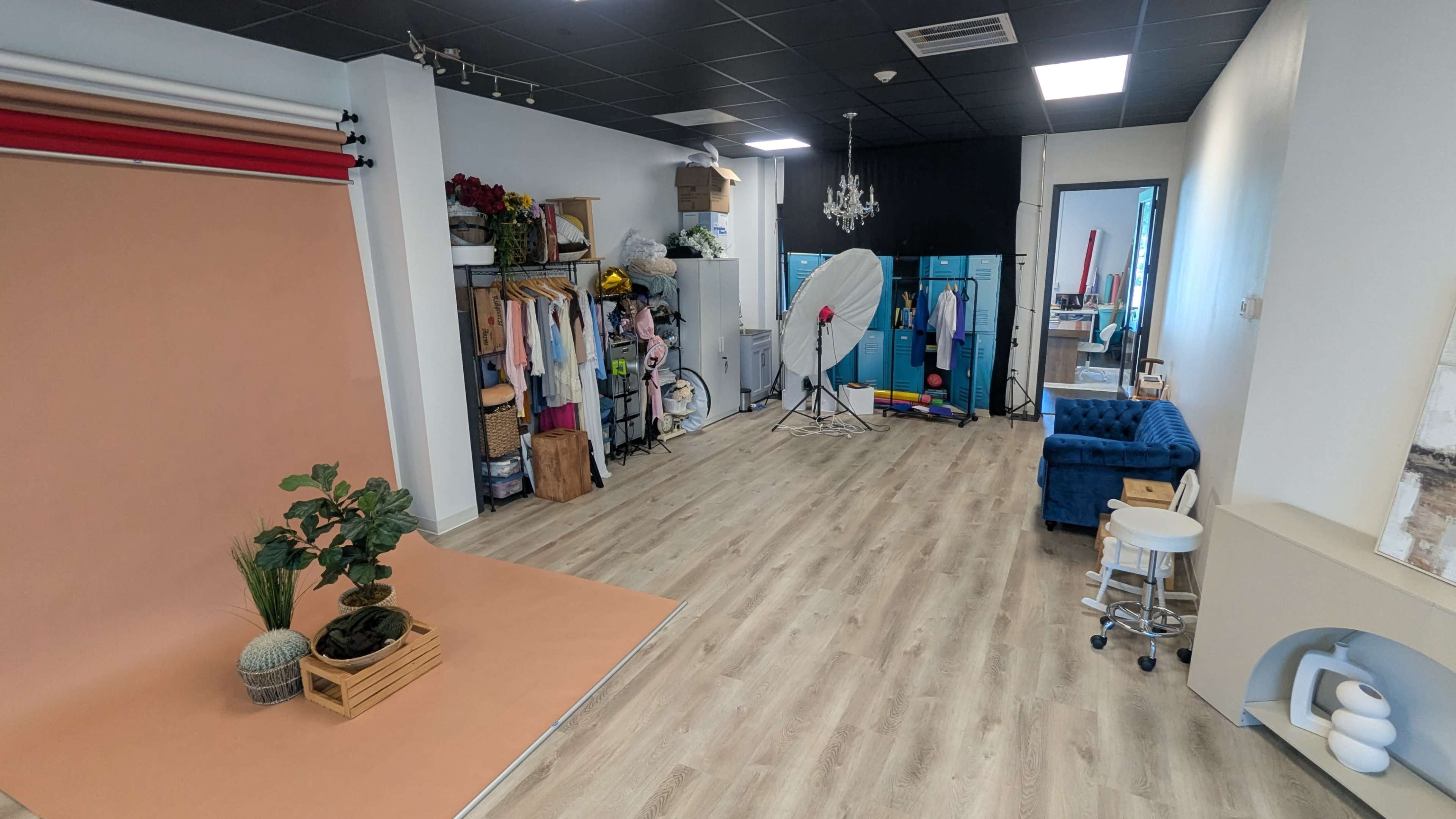 The image shows a spacious studio with various backdrops, photography equipment, and a blue couch, arranged for photo shoots.