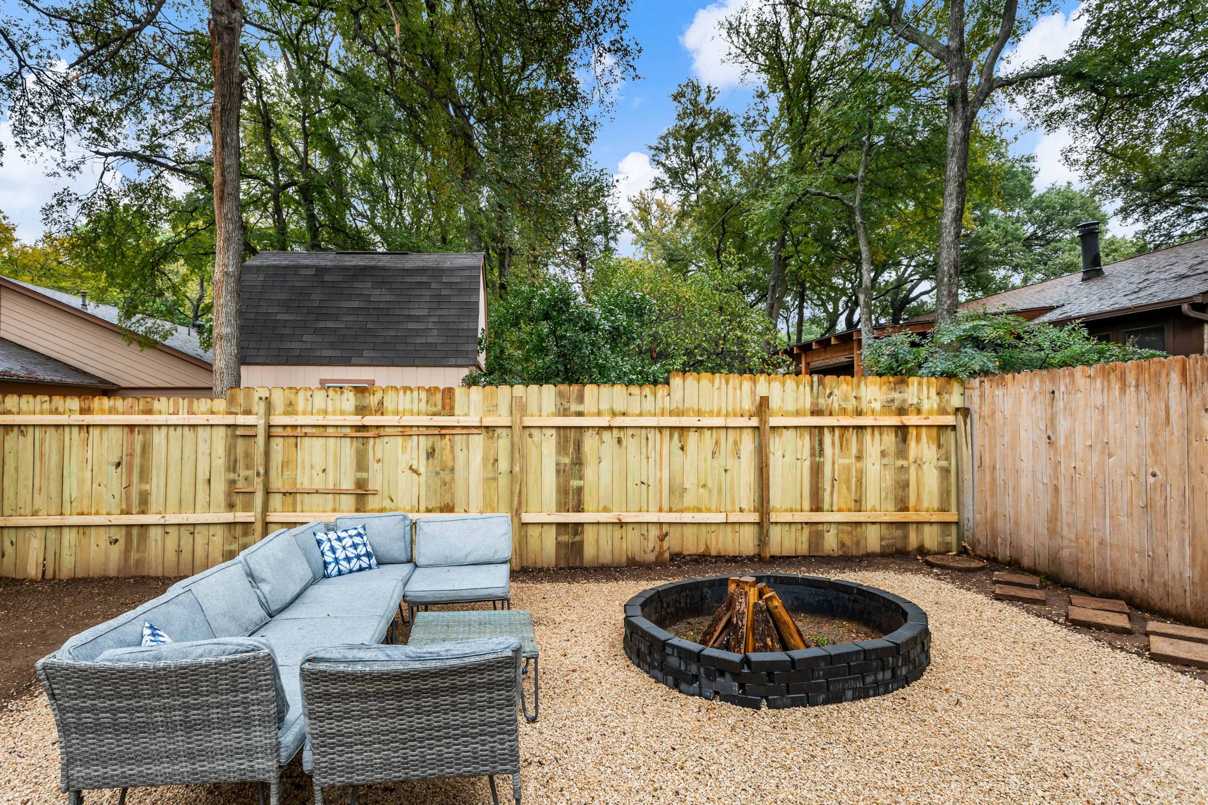 A fenced backyard featuring a circular fire pit surrounded by gravel and a sectional outdoor couch.