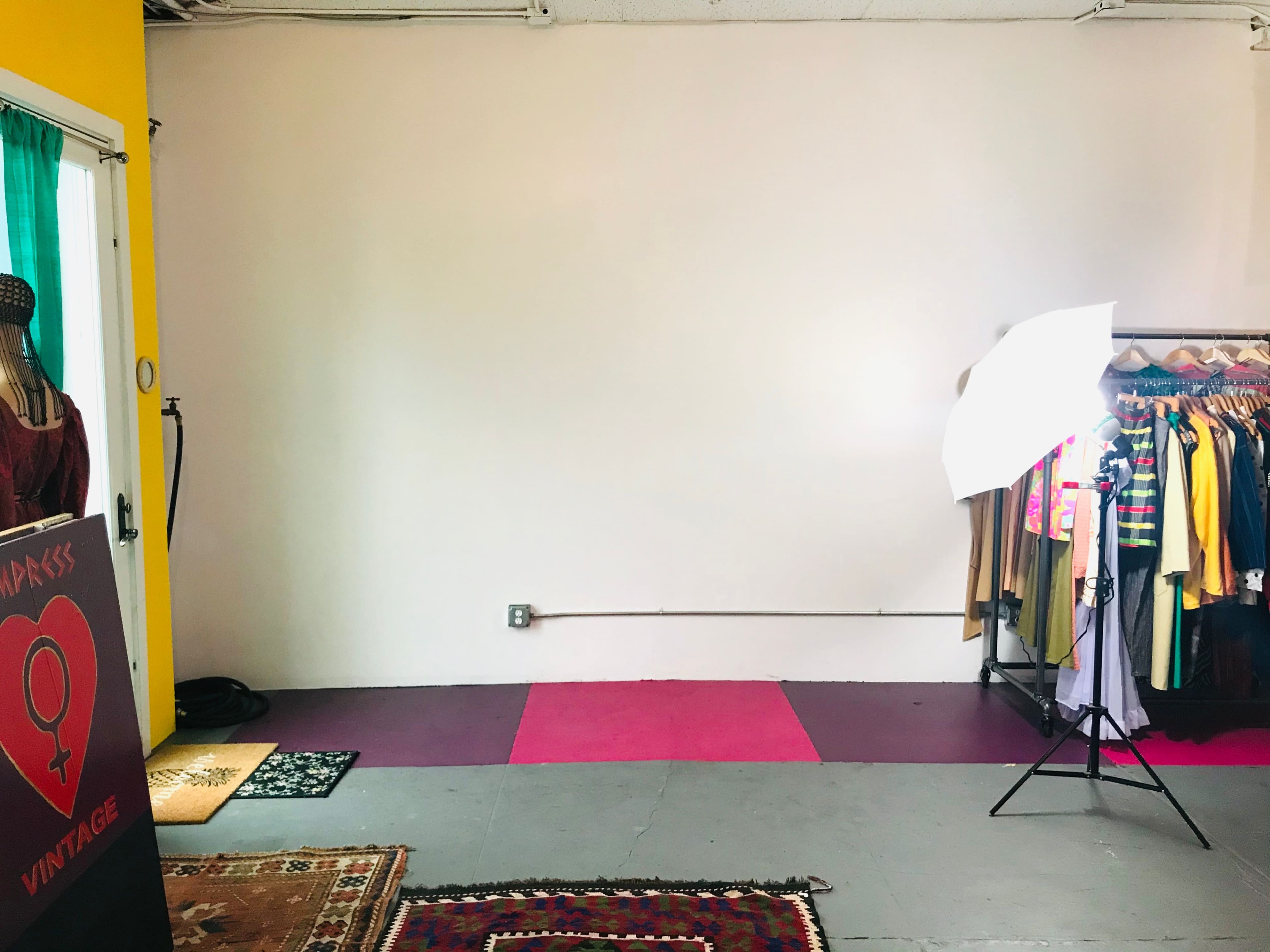 A brightly lit vintage clothing store with racks of clothes along one wall and an empty space with a backdrop and lighting setup.