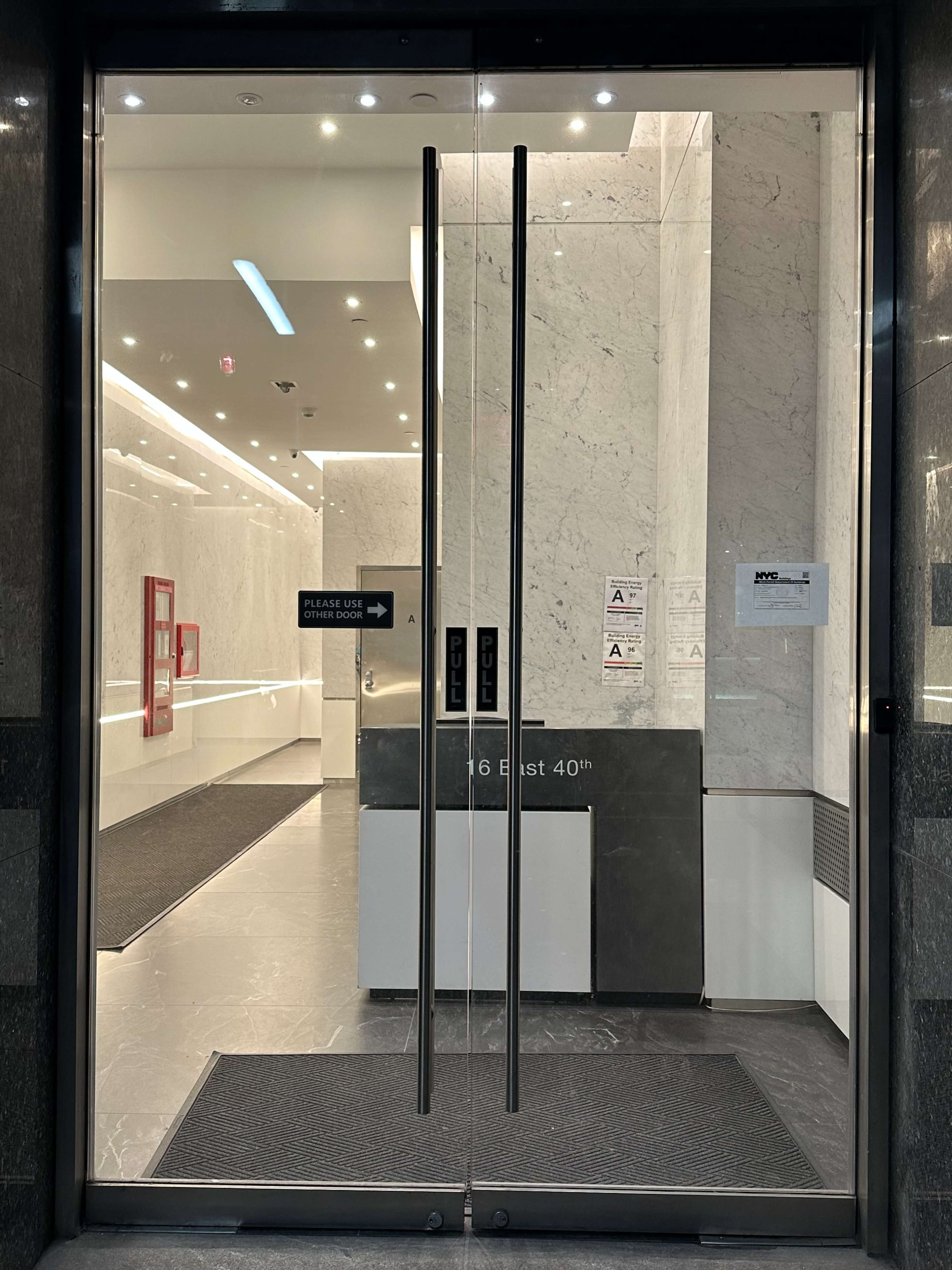 The image shows the entrance of a modern building with glass double doors and a marble interior.