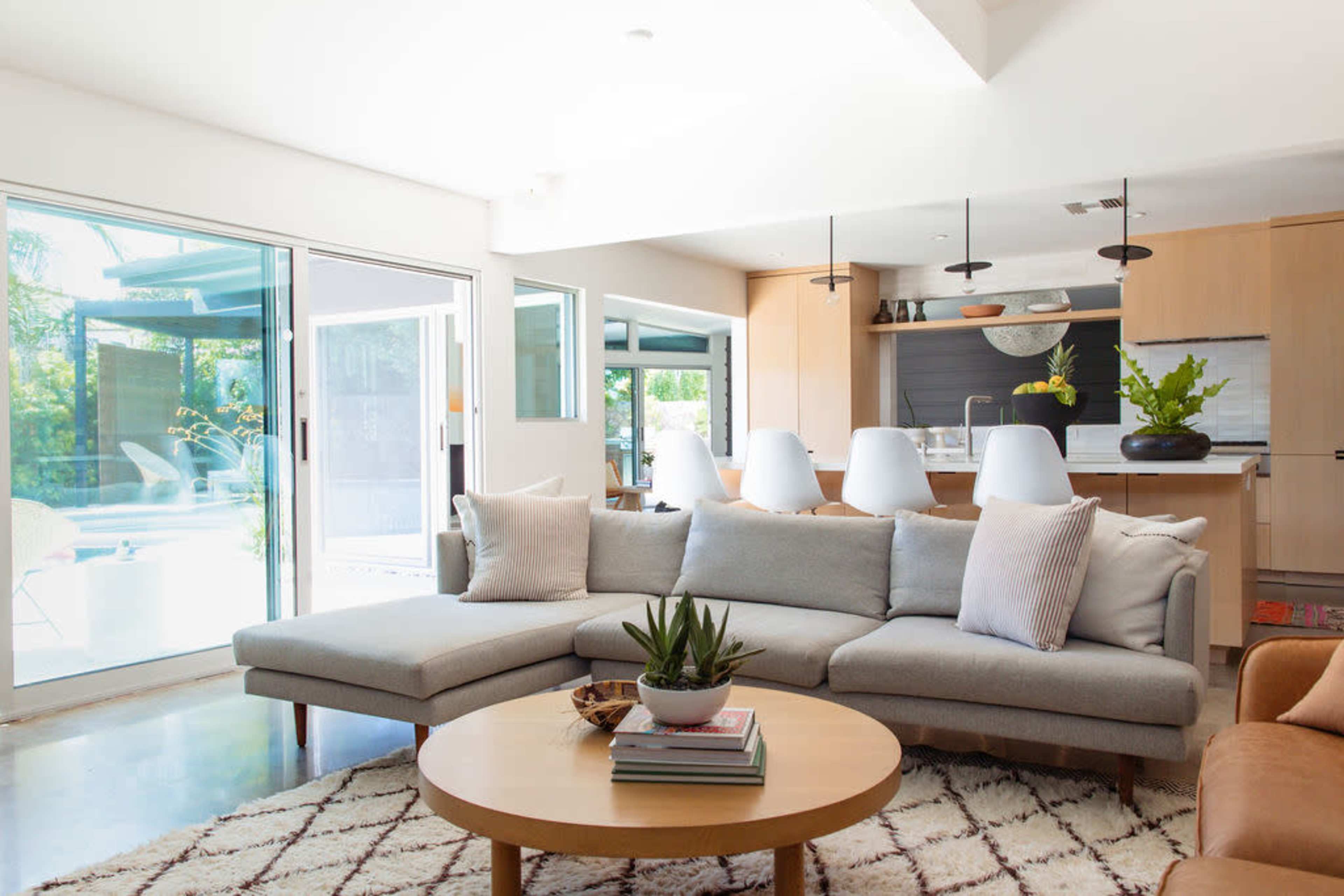The living room features a gray sectional sofa, a round wooden coffee table, and large glass doors leading to an outdoor area with a swimming pool.