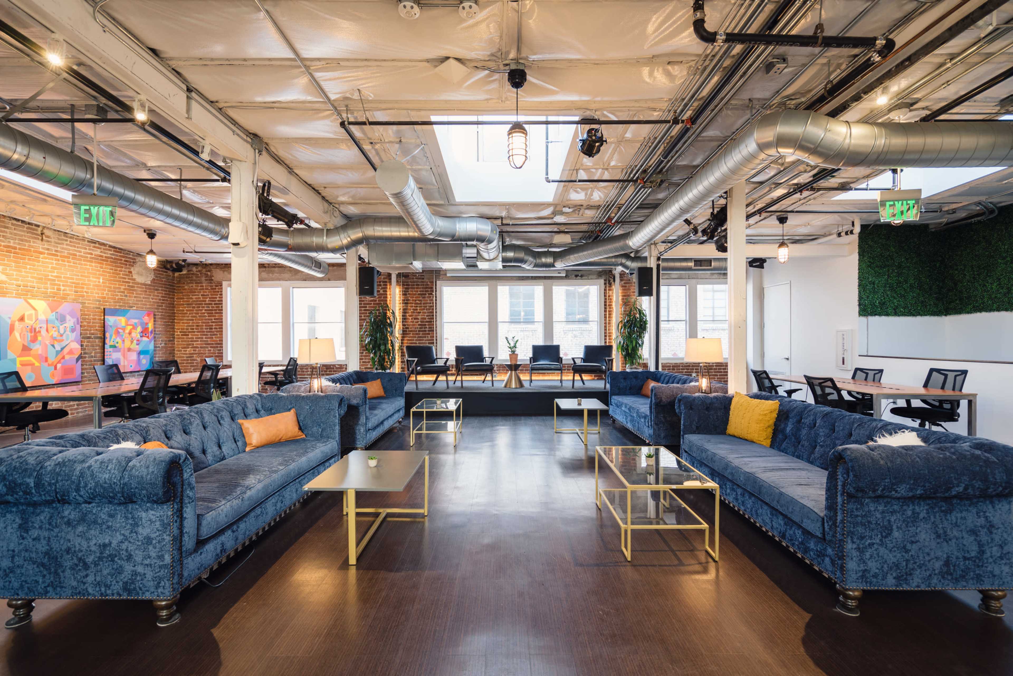 A spacious lounge area with two blue tufted sofas, glass coffee tables, and large windows letting in natural light.
