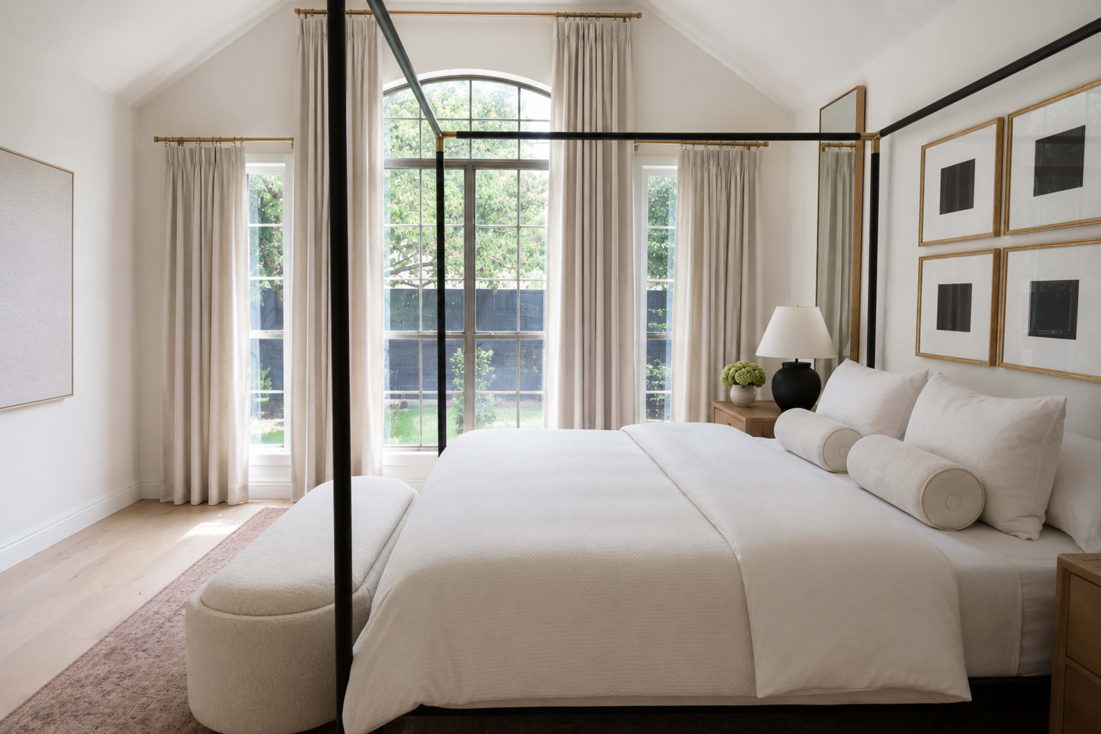 The image depicts a modern bedroom featuring a four-poster bed, large windows with flowing curtains, and a minimalist decor style.