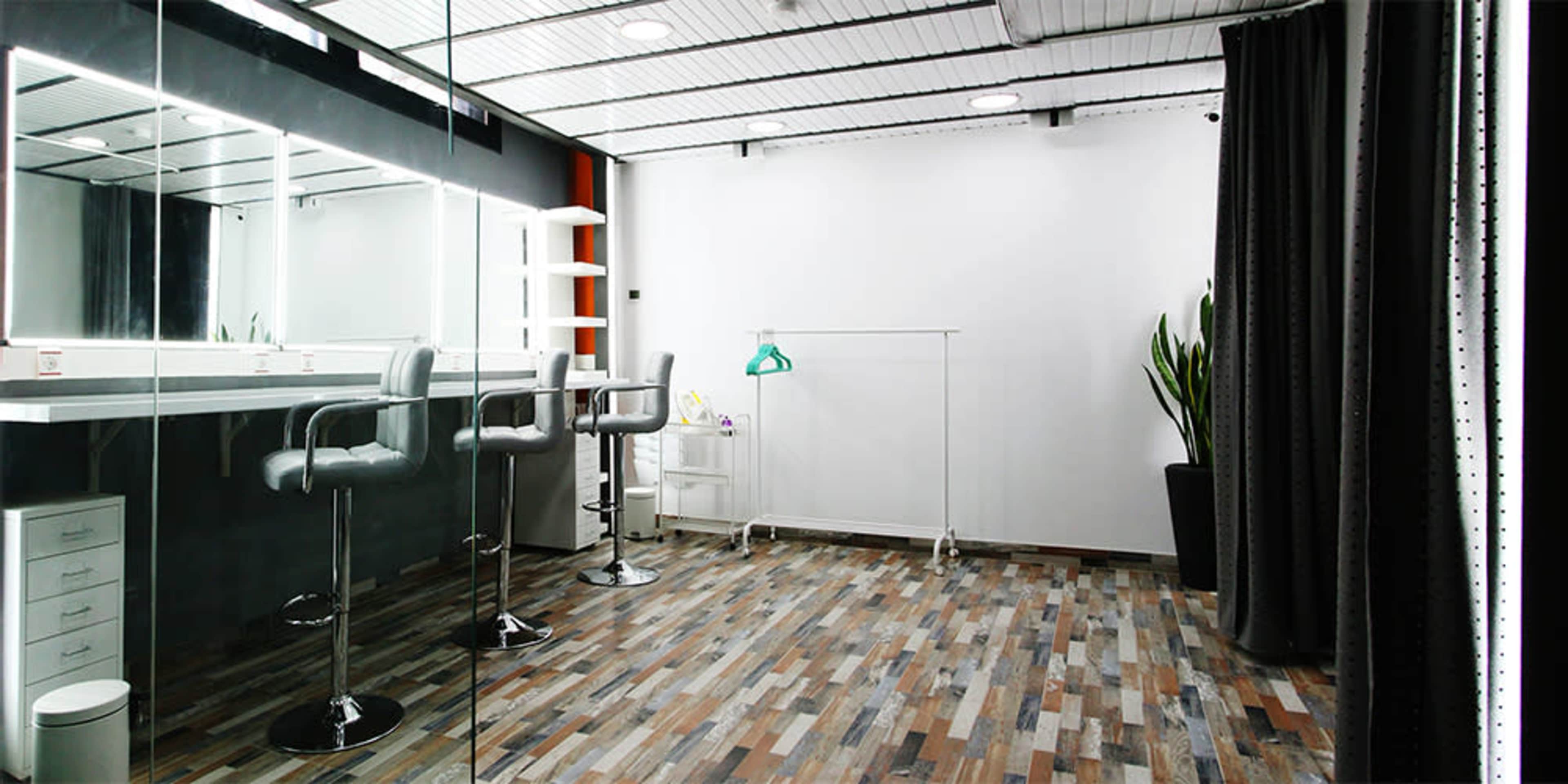 A modern dressing room with a mirrored wall, two barstools, and a clothing rack against a white background.