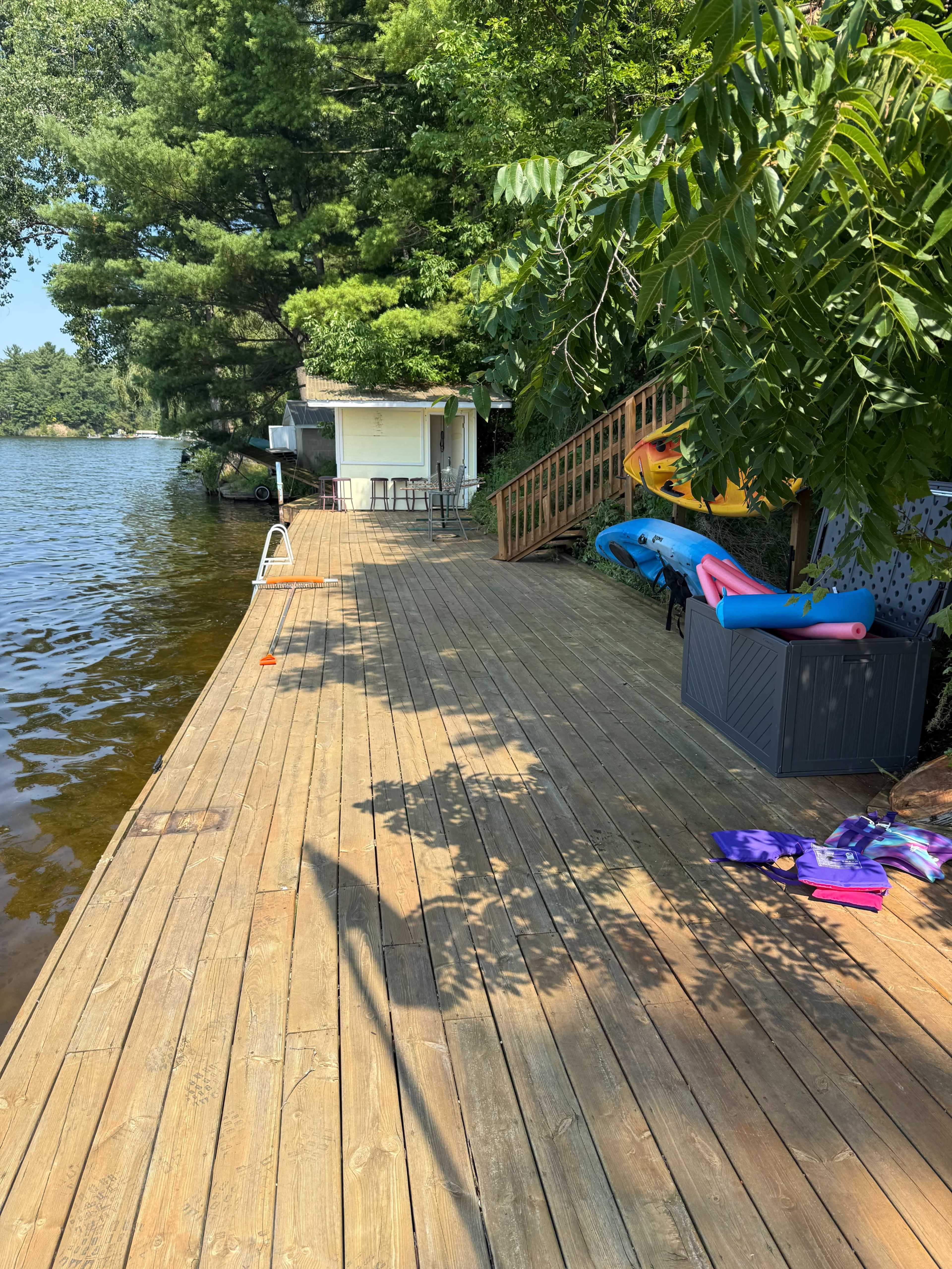 A wooden dock extends beside a calm lake, with a storage box and colorful kayaks positioned near the water's edge.