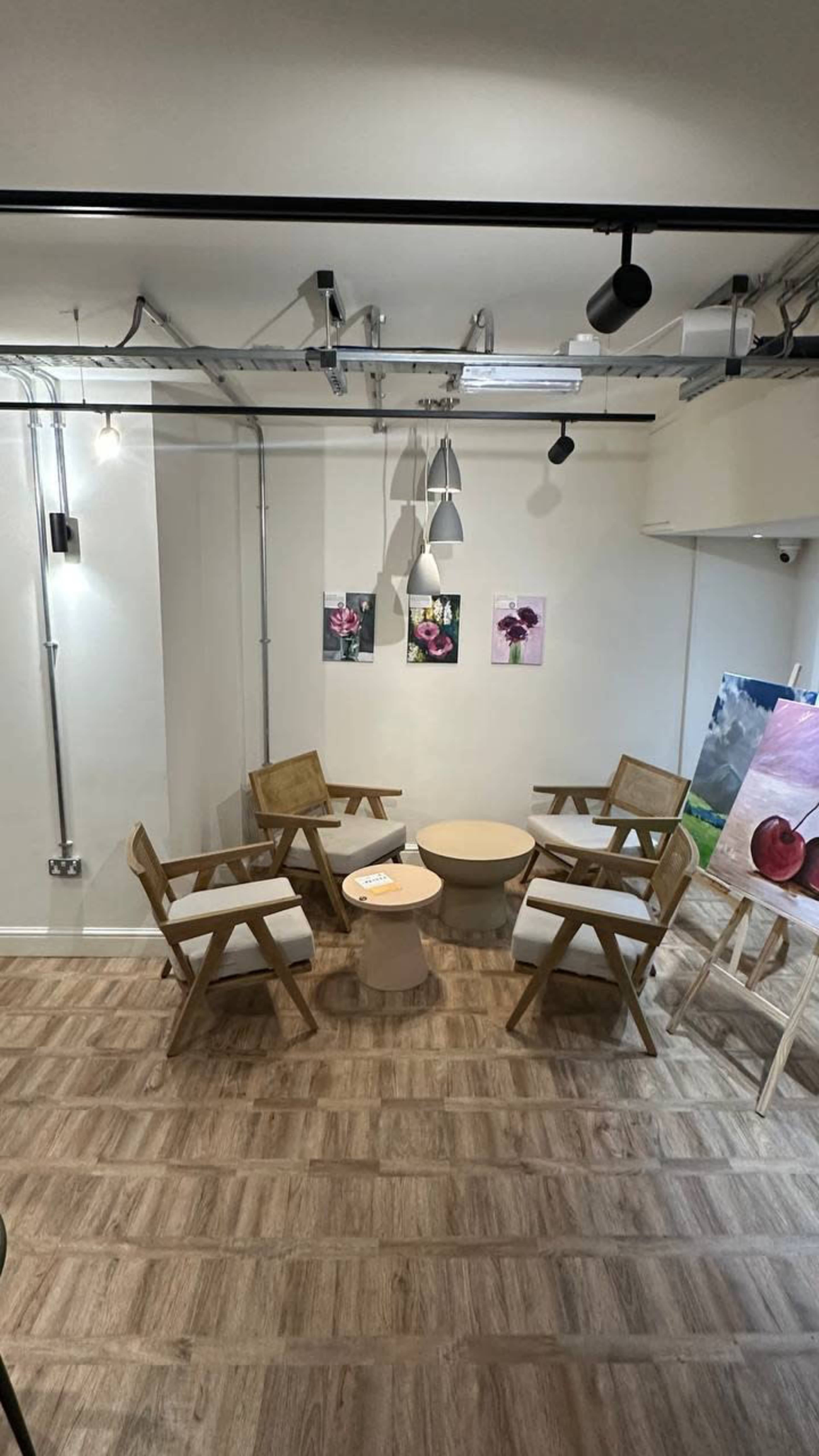 The image shows a small indoor seating area with wooden chairs arranged around a circular table and artwork on the walls.