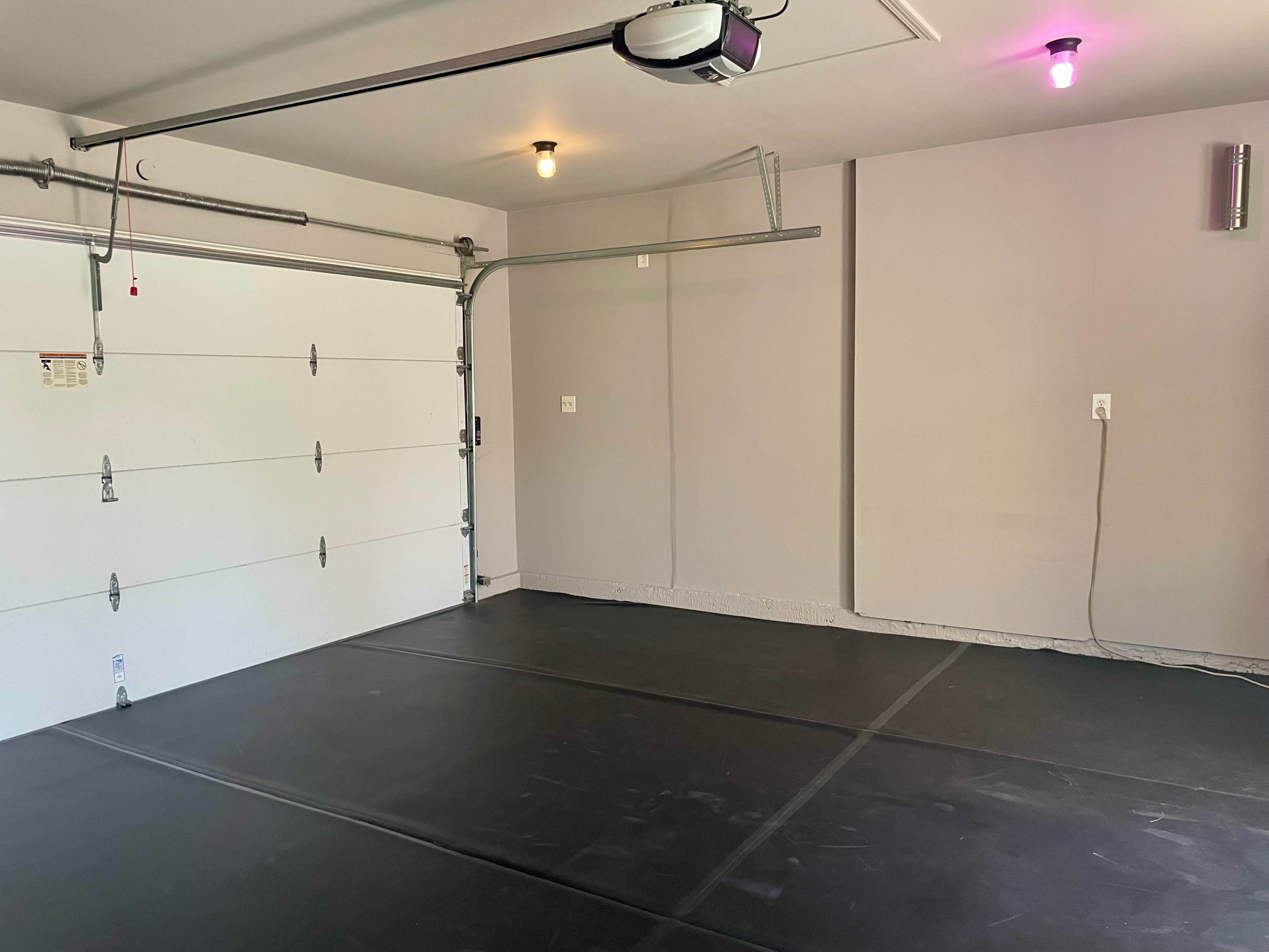 A clean, empty garage features a white garage door, gray walls, and a dark floor.