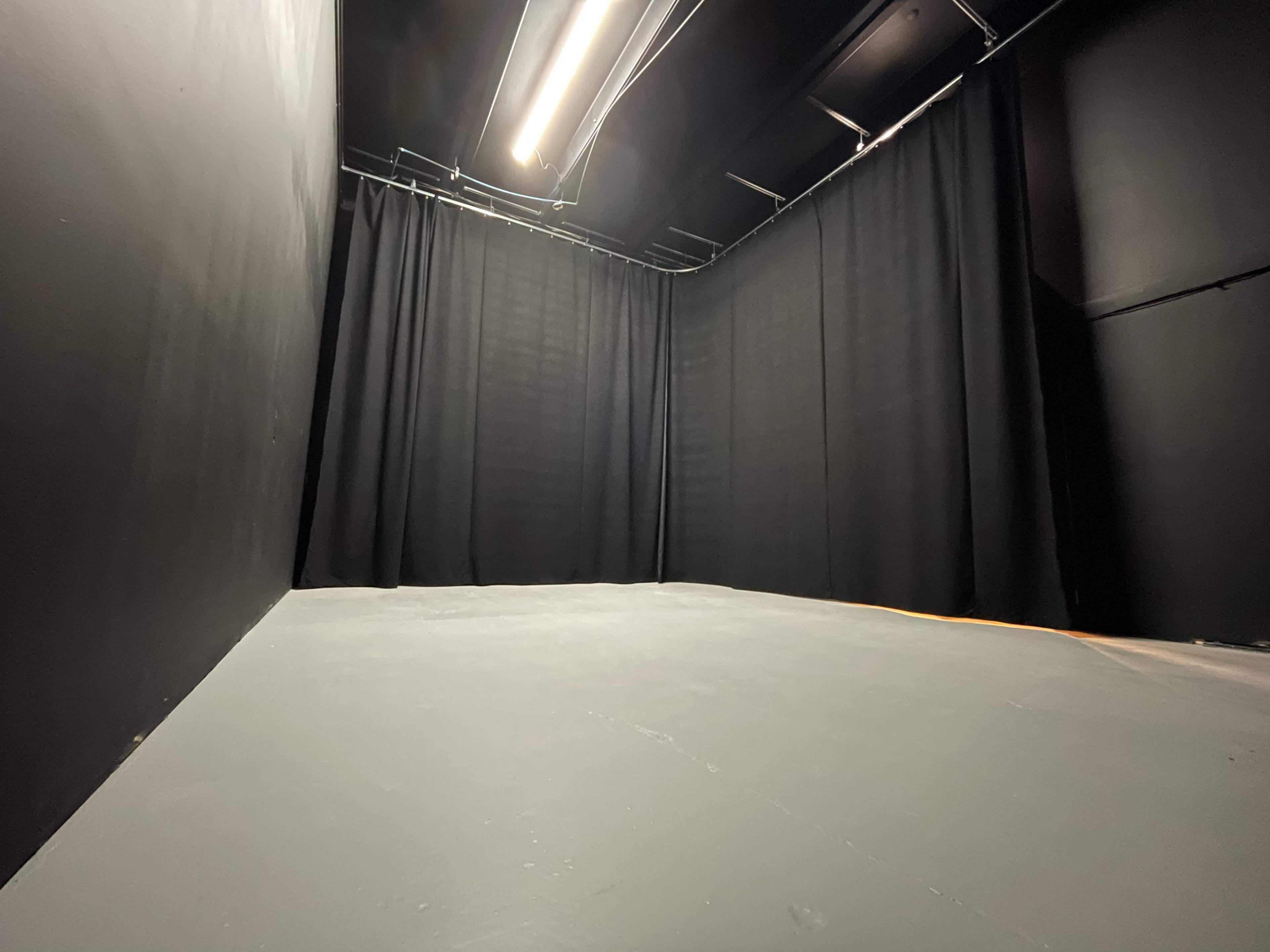 The image shows a dimly lit room with black curtains and a gray floor.