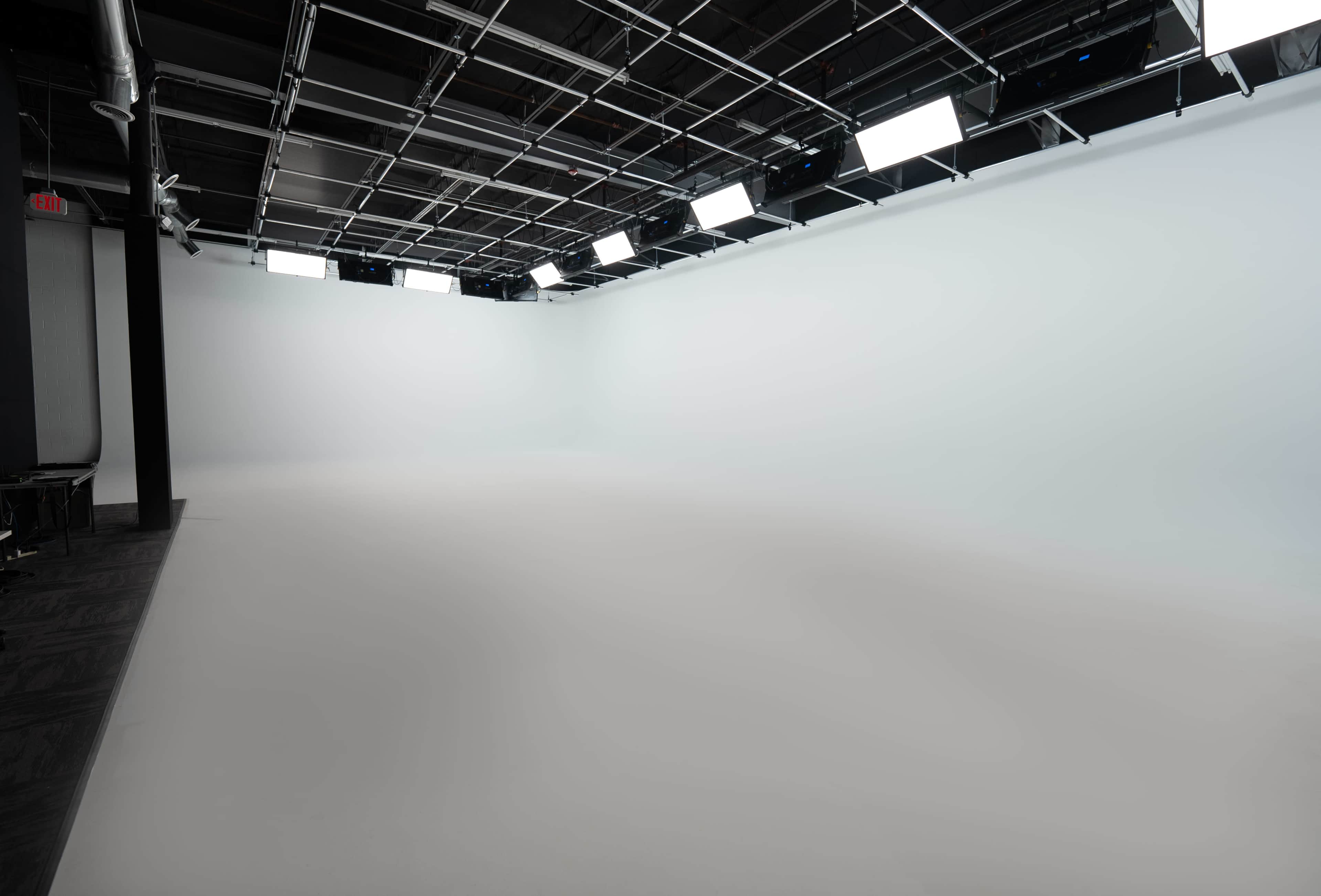An empty studio space with a light gray floor and overhead lighting.