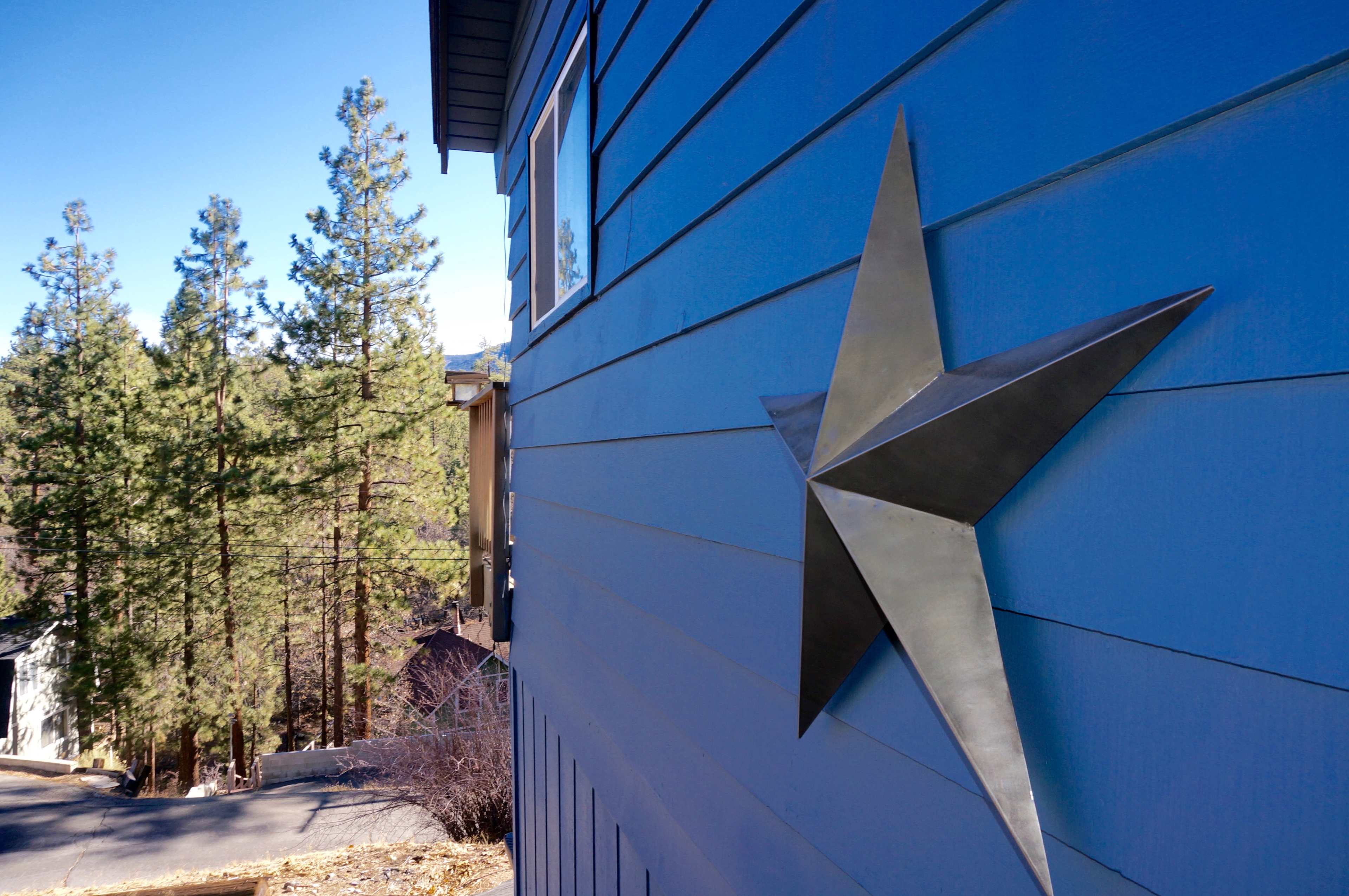 A large metal star is mounted on the blue exterior of a building, with evergreen trees in the background.