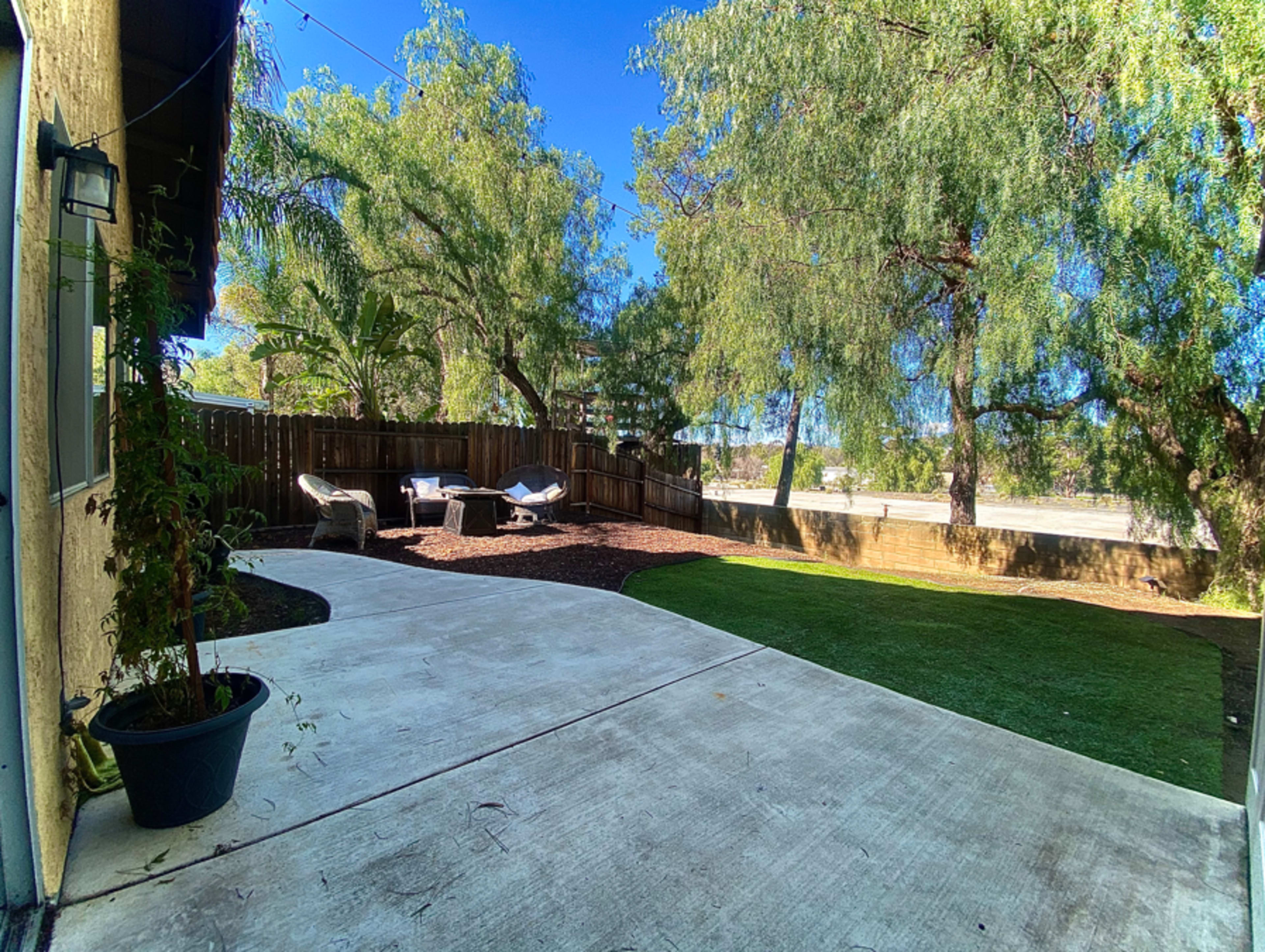 A concrete patio leads to a grassy yard surrounded by trees and a wooden fence.