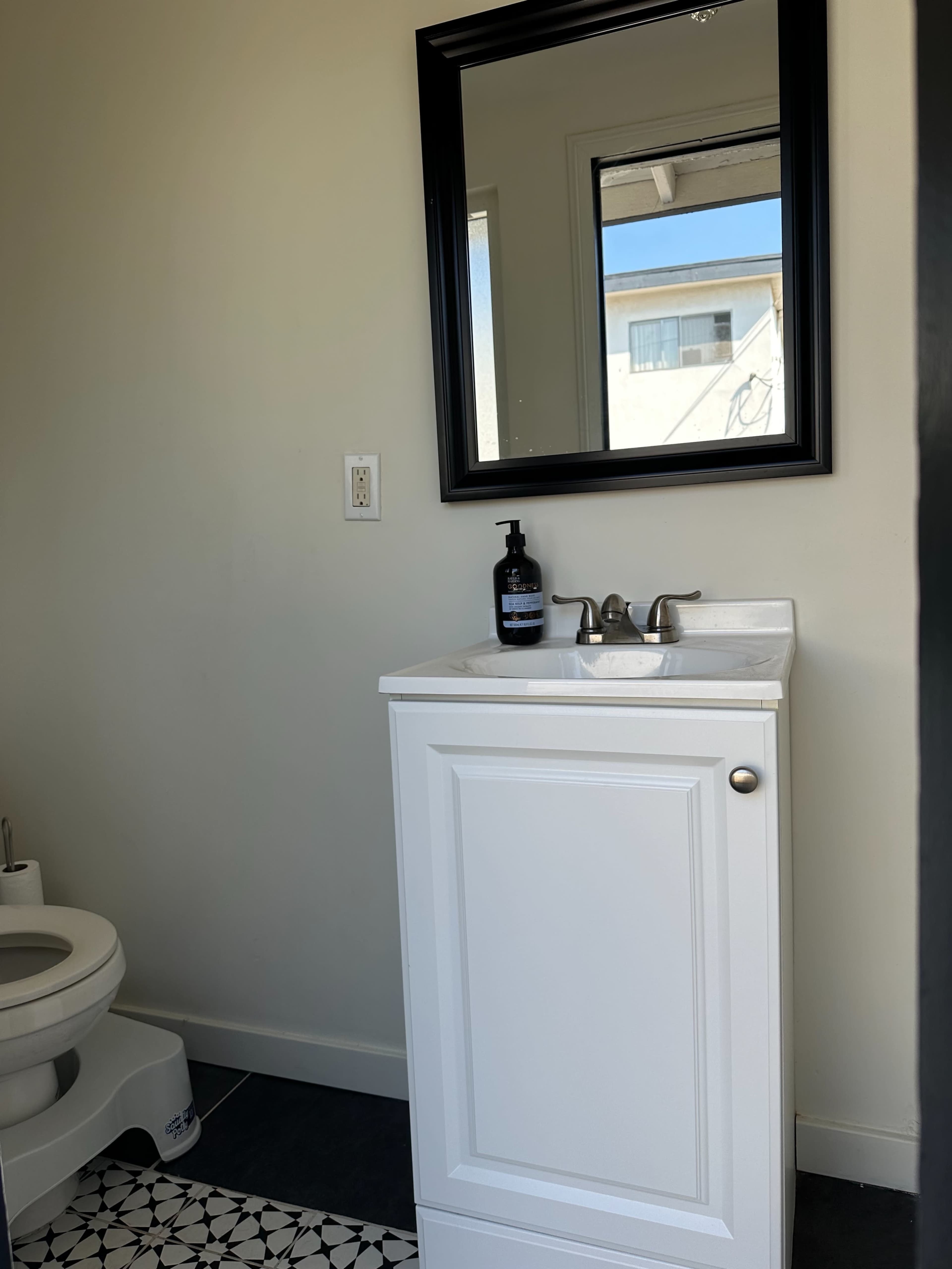 A small bathroom features a toilet and a white cabinet with a sink beneath a mirror.